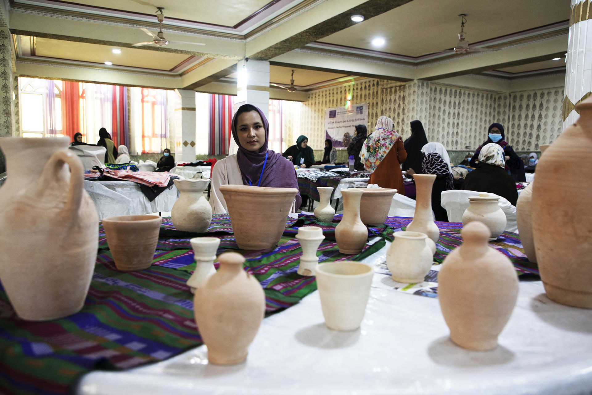 A woman sits among various clay pottery pieces in an indoor setting.