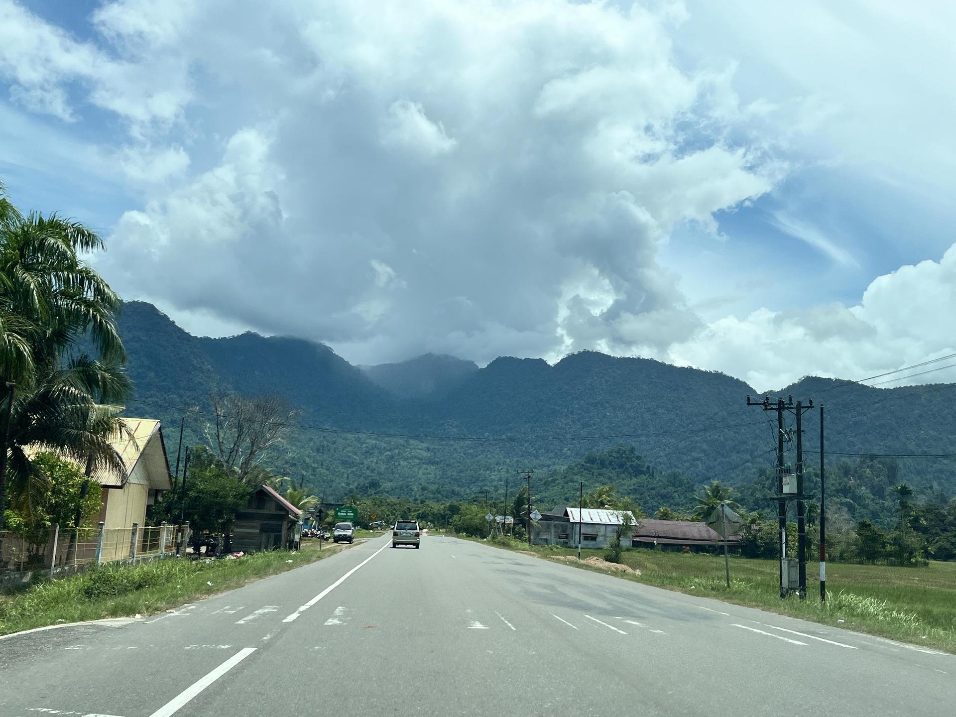 Scenic highway with mountains in the background and lush greenery along the roadside.