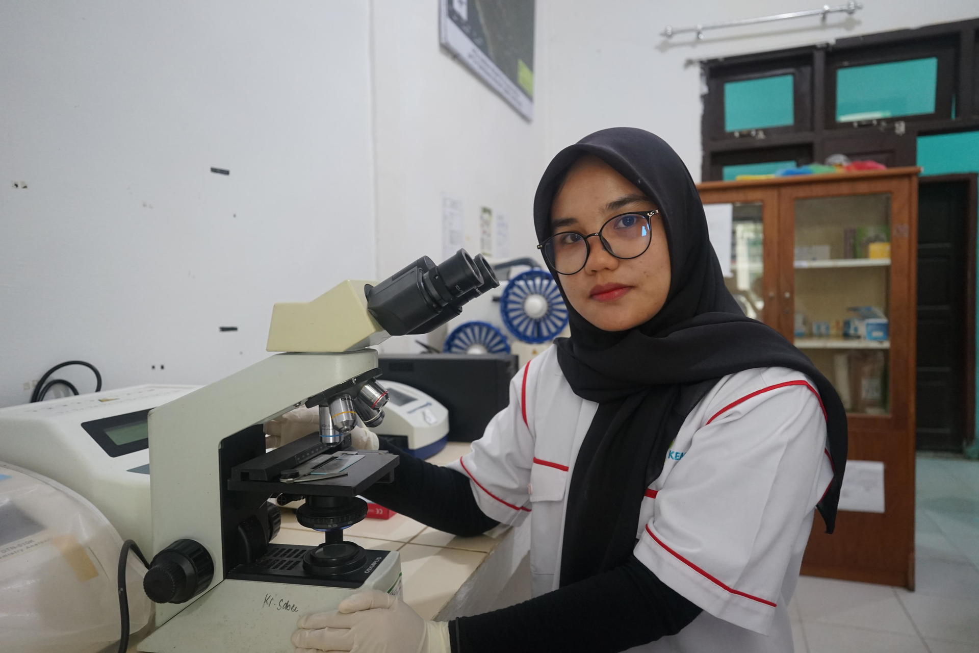 A woman in a lab coat uses a microscope in a bright laboratory setting.