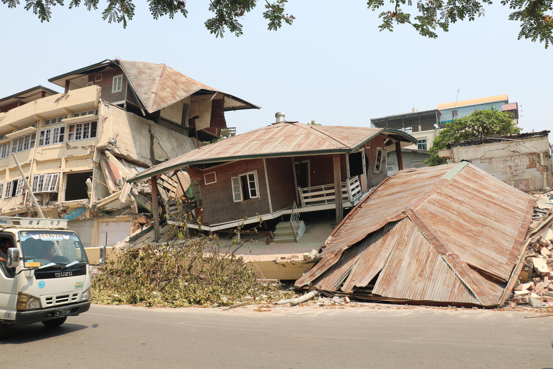Buildings damaged by an earthquake, with debris and a tilted roof in the foreground.