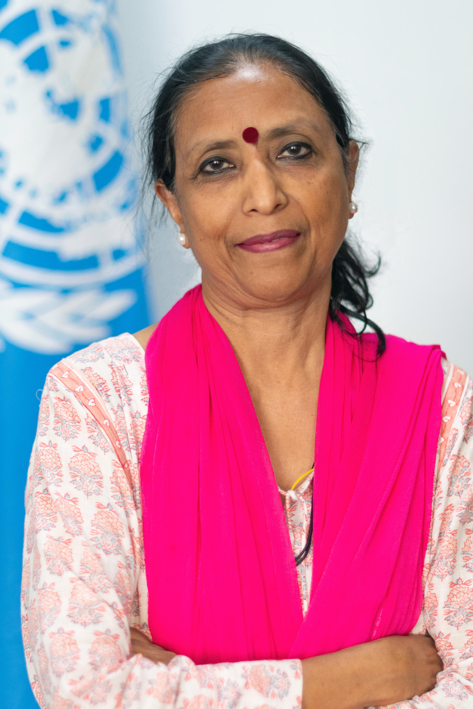 A woman in traditional attire stands confidently with crossed arms, smiling softly.