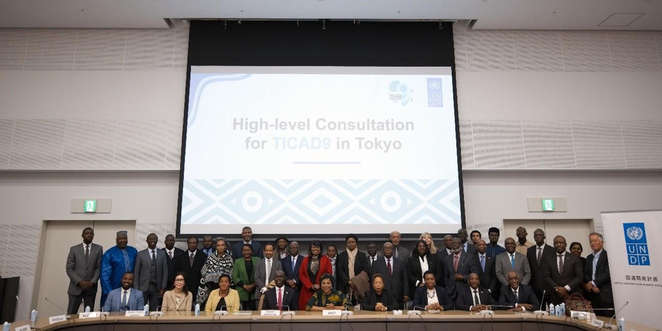 Group of individuals posing for a photo at a conference in Tokyo, with a presentation screen behind them.