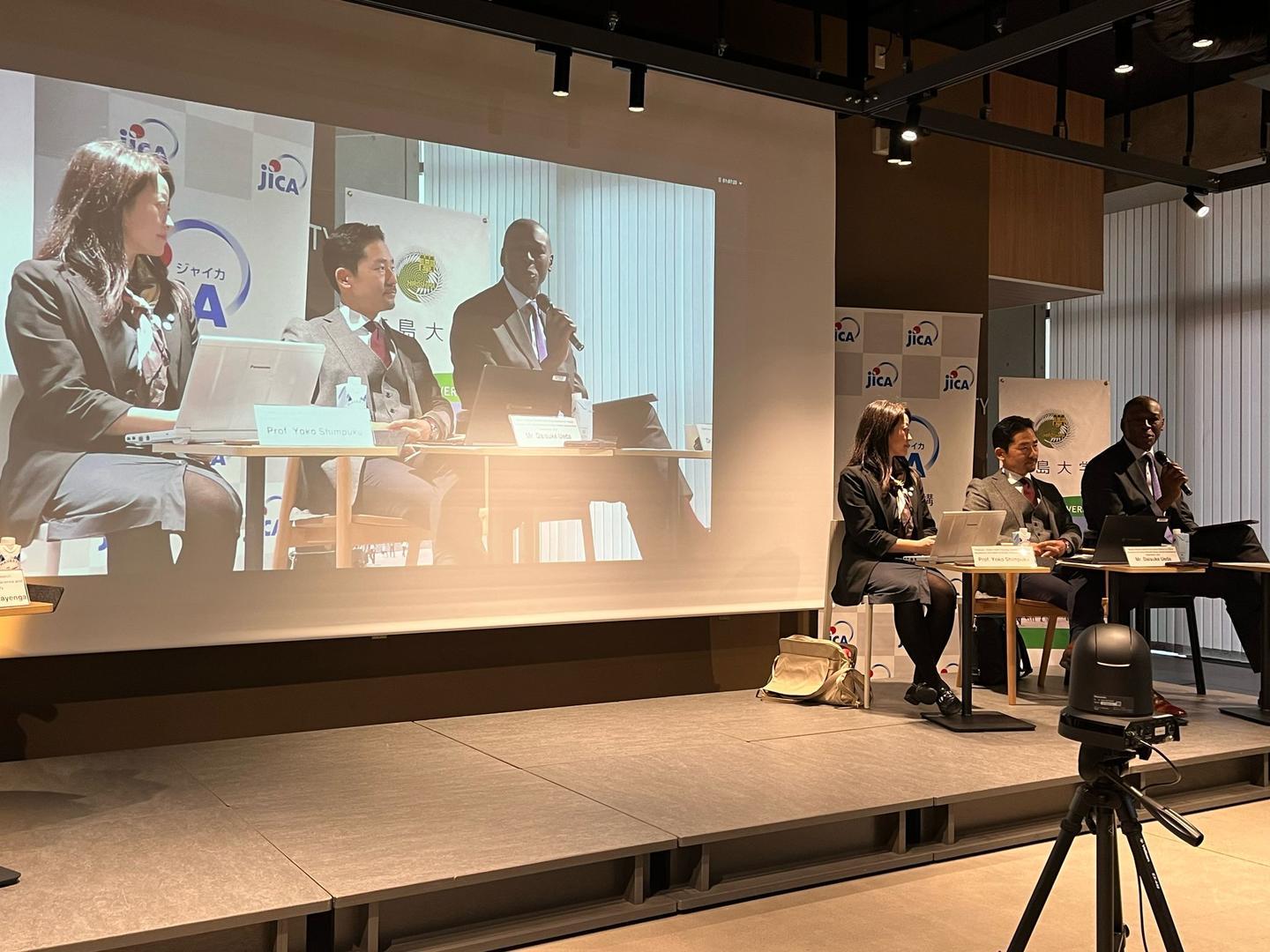 Panel discussion with four speakers at a conference, with a projection behind them.
