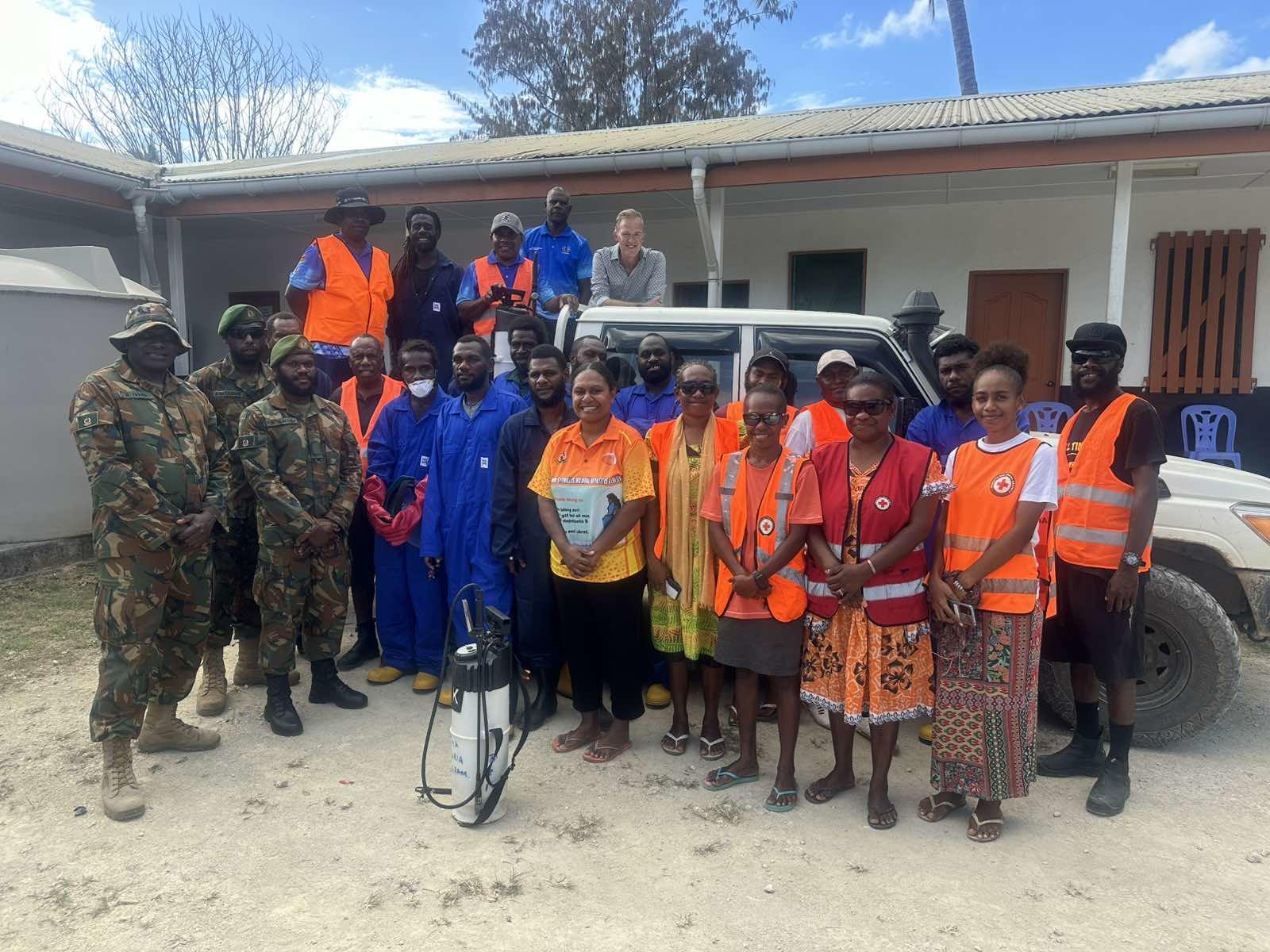 A diverse group of people in uniforms and colorful attire, posing together near a vehicle.