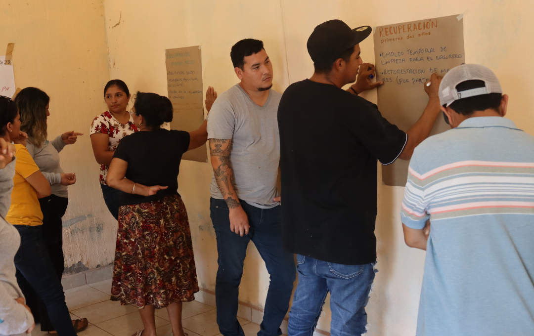 A diverse group of people writing on papers mounted on a wall in a bright room.
