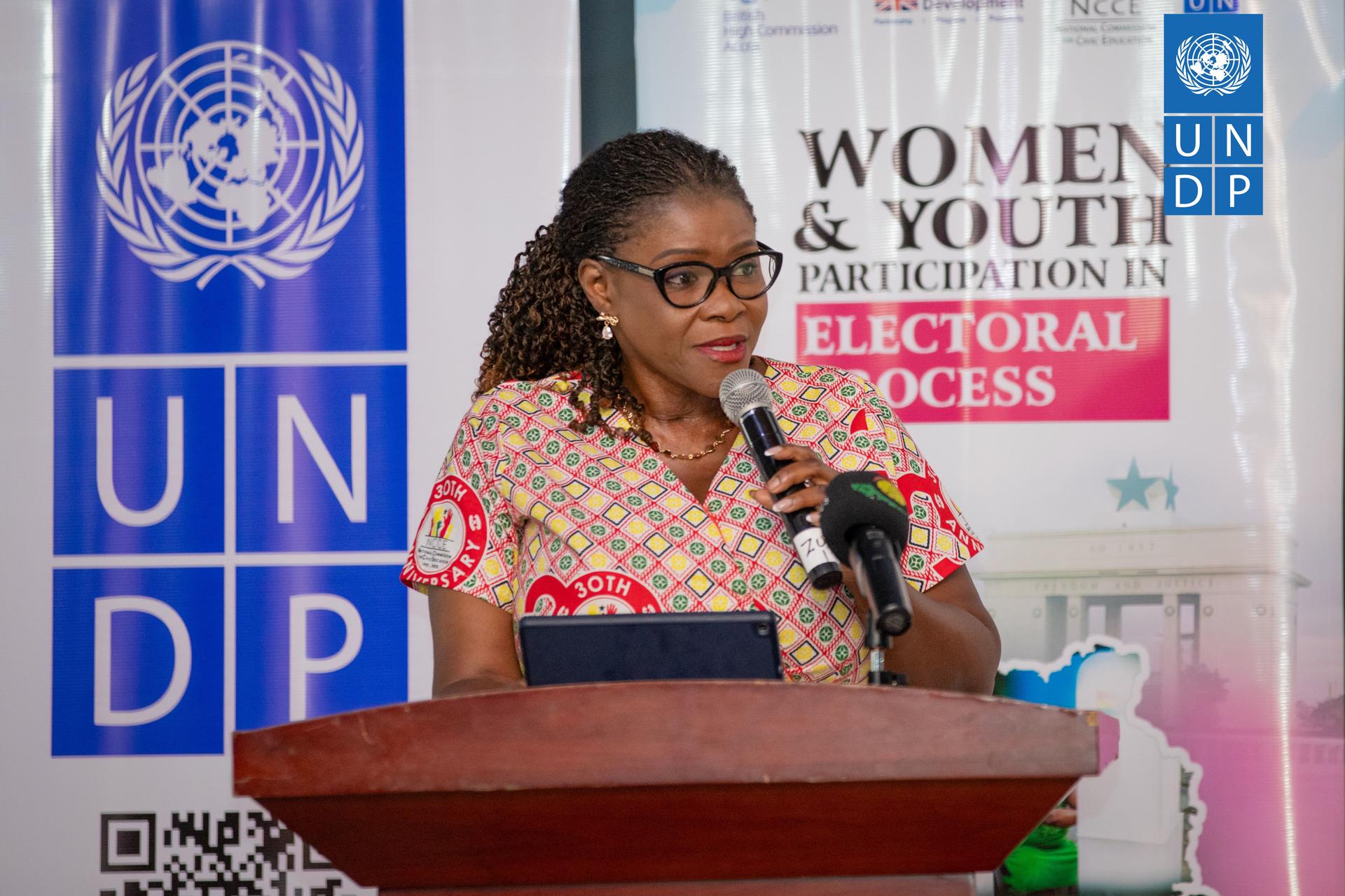 A woman speaks into a microphone at a podium, with UNDP branding in the background.