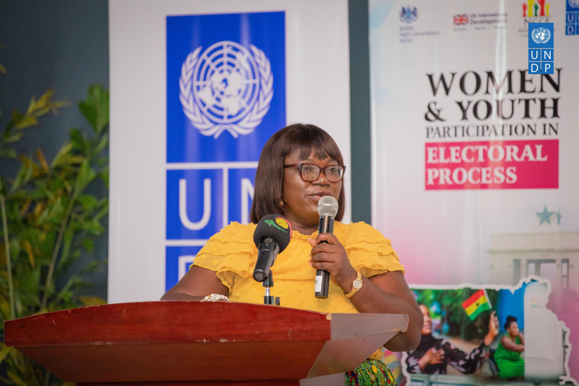 A woman speaking at a podium with a UN logo in the background, promoting youth involvement.