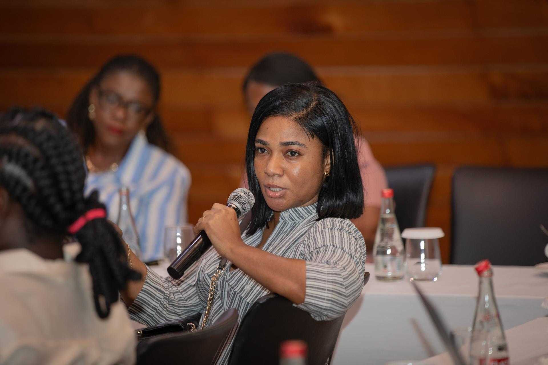A woman speaking into a microphone at a conference, engaged and looking confident.