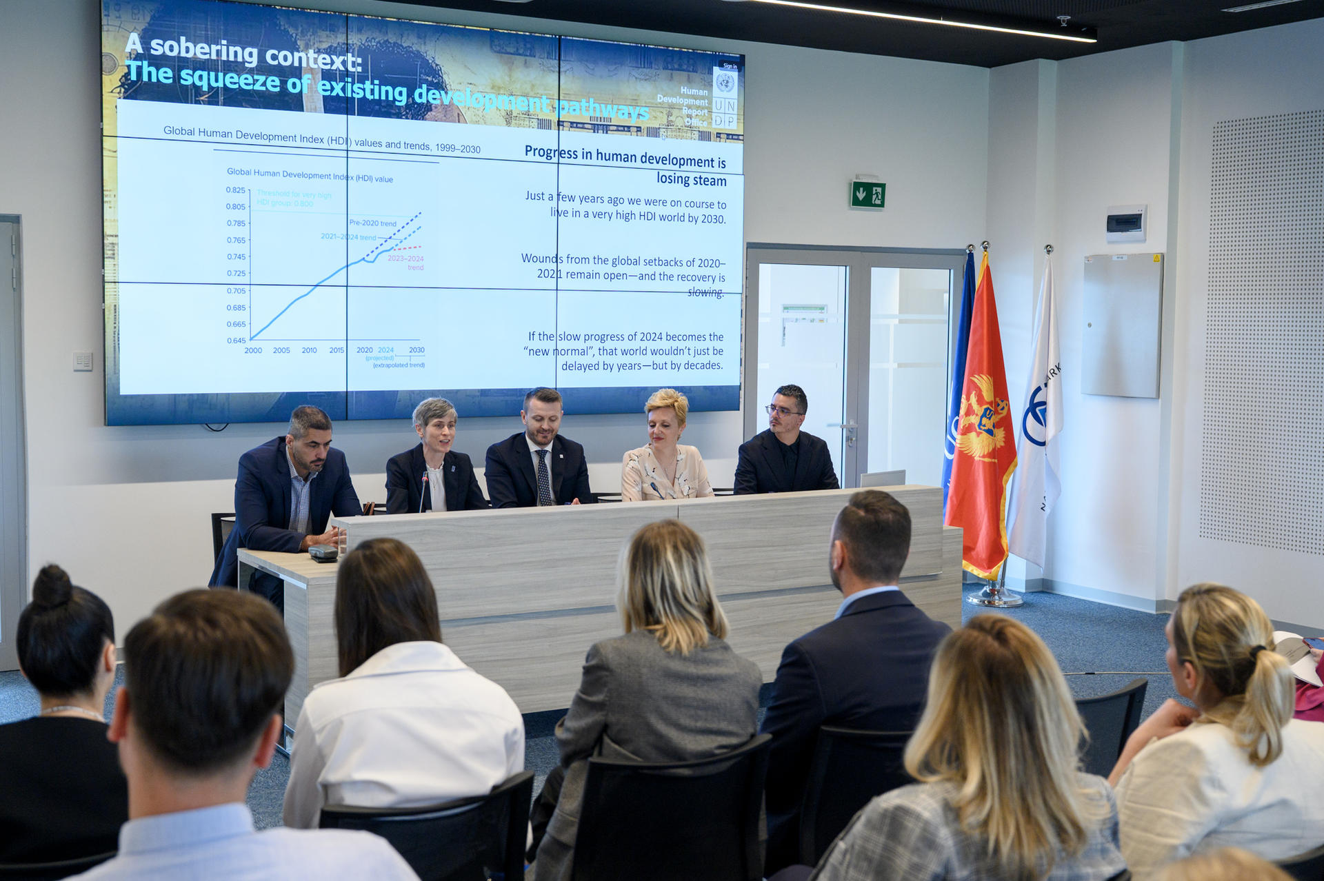 A conference scene with speakers at a table and an audience in a modern room.