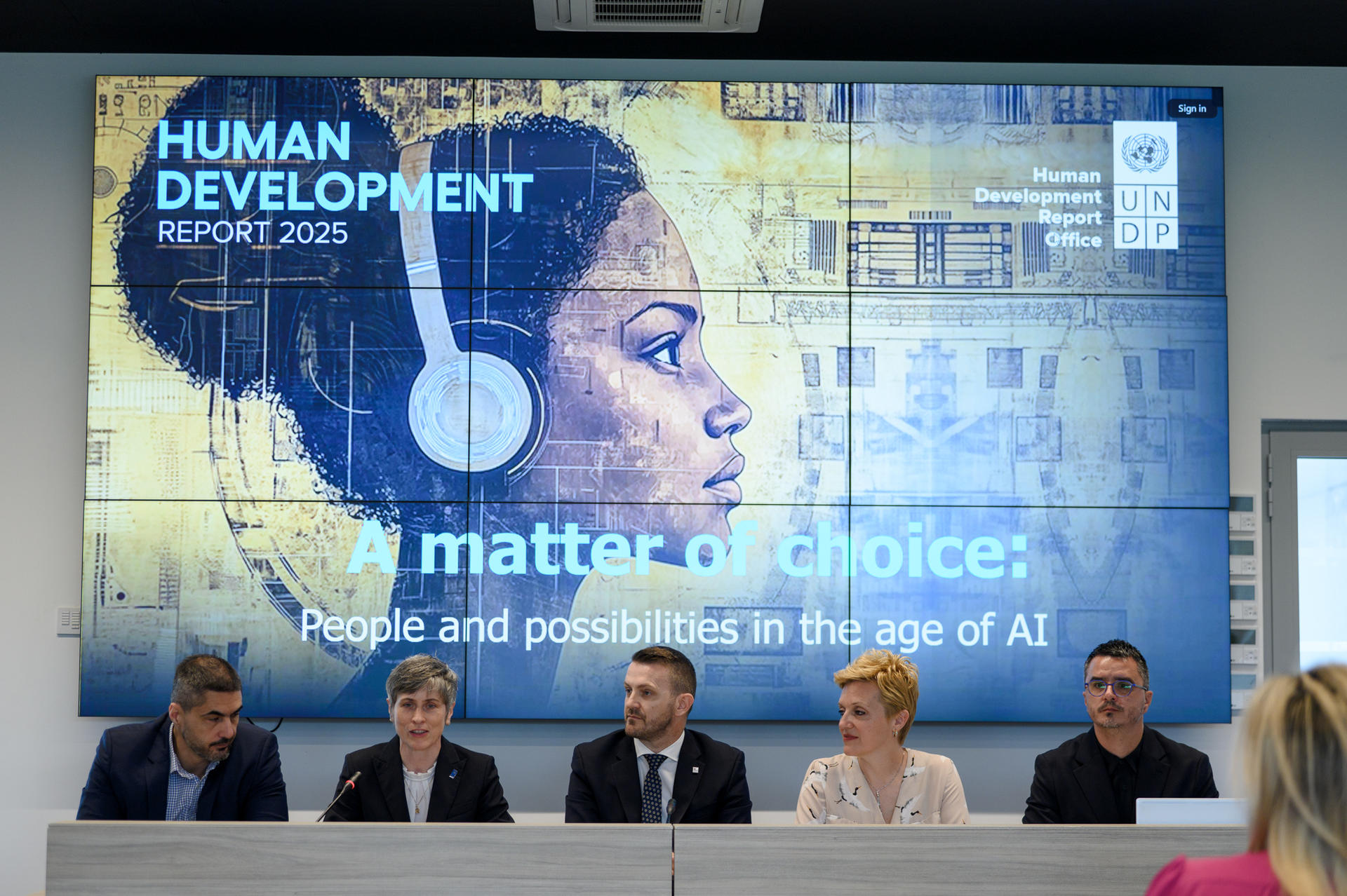 Panel discussion at event with a large screen displaying a woman's profile and text on AI.