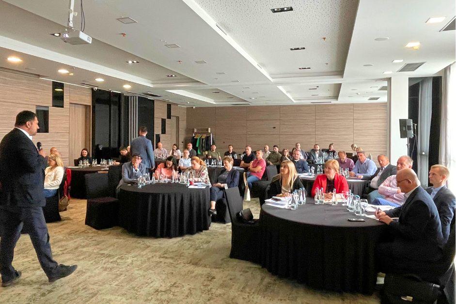 A conference room filled with seated participants, listening to a presenter.