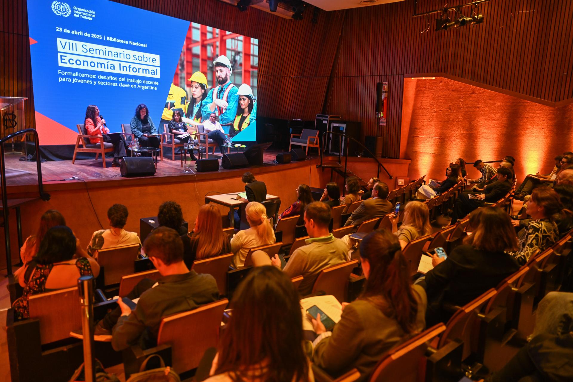 Un panel de discusión en un escenario con una audiencia atenta en una sala de conferencias.
