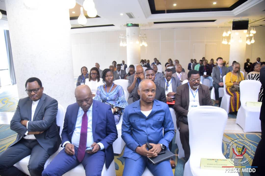 A diverse audience seated in a conference room, attentively listening to a speaker.