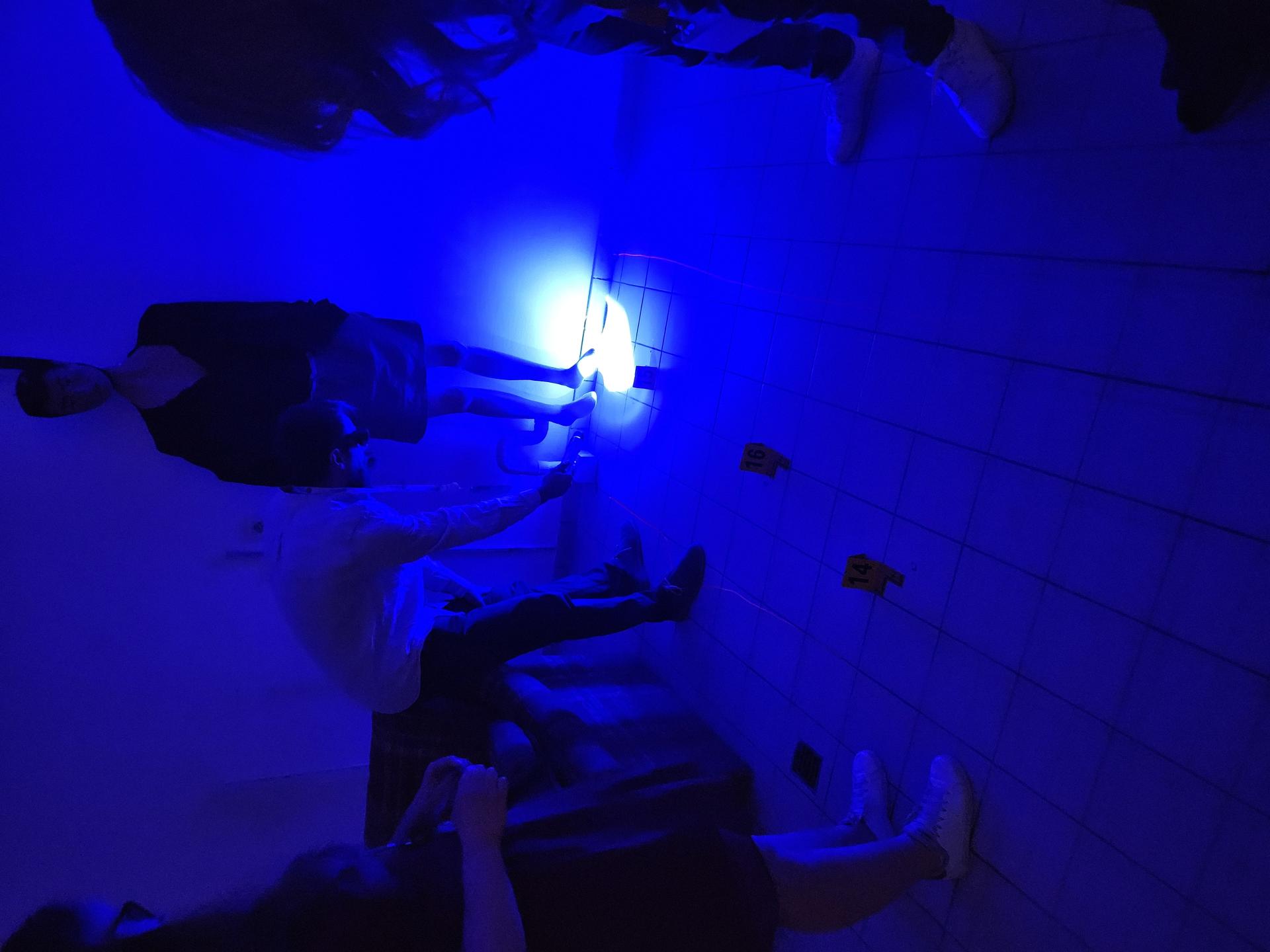 Group of people in a dimly lit, blue room, examining an object on the floor.