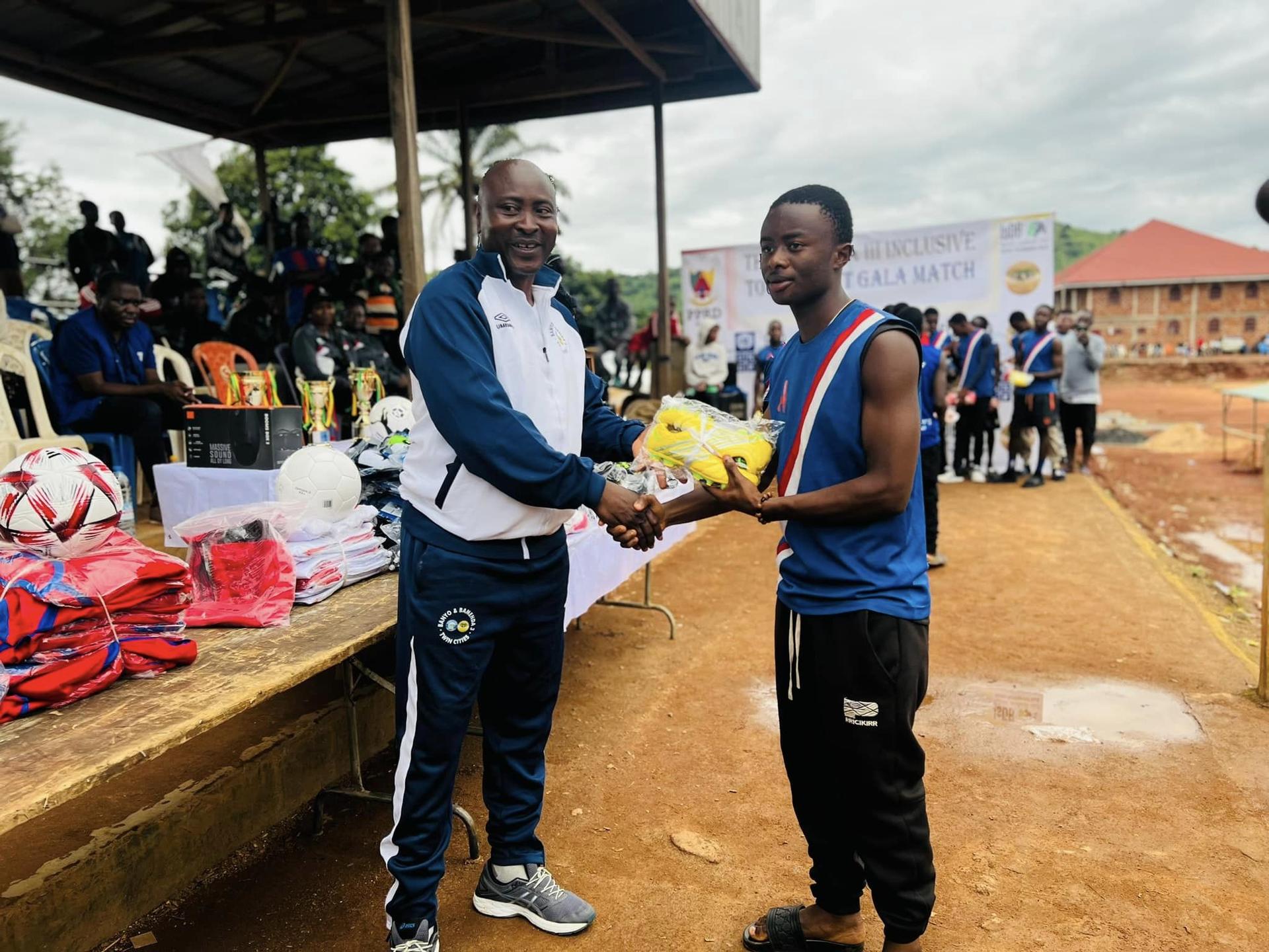 A man in sportswear shakes hands with another man, receiving an award in a sports event setting.