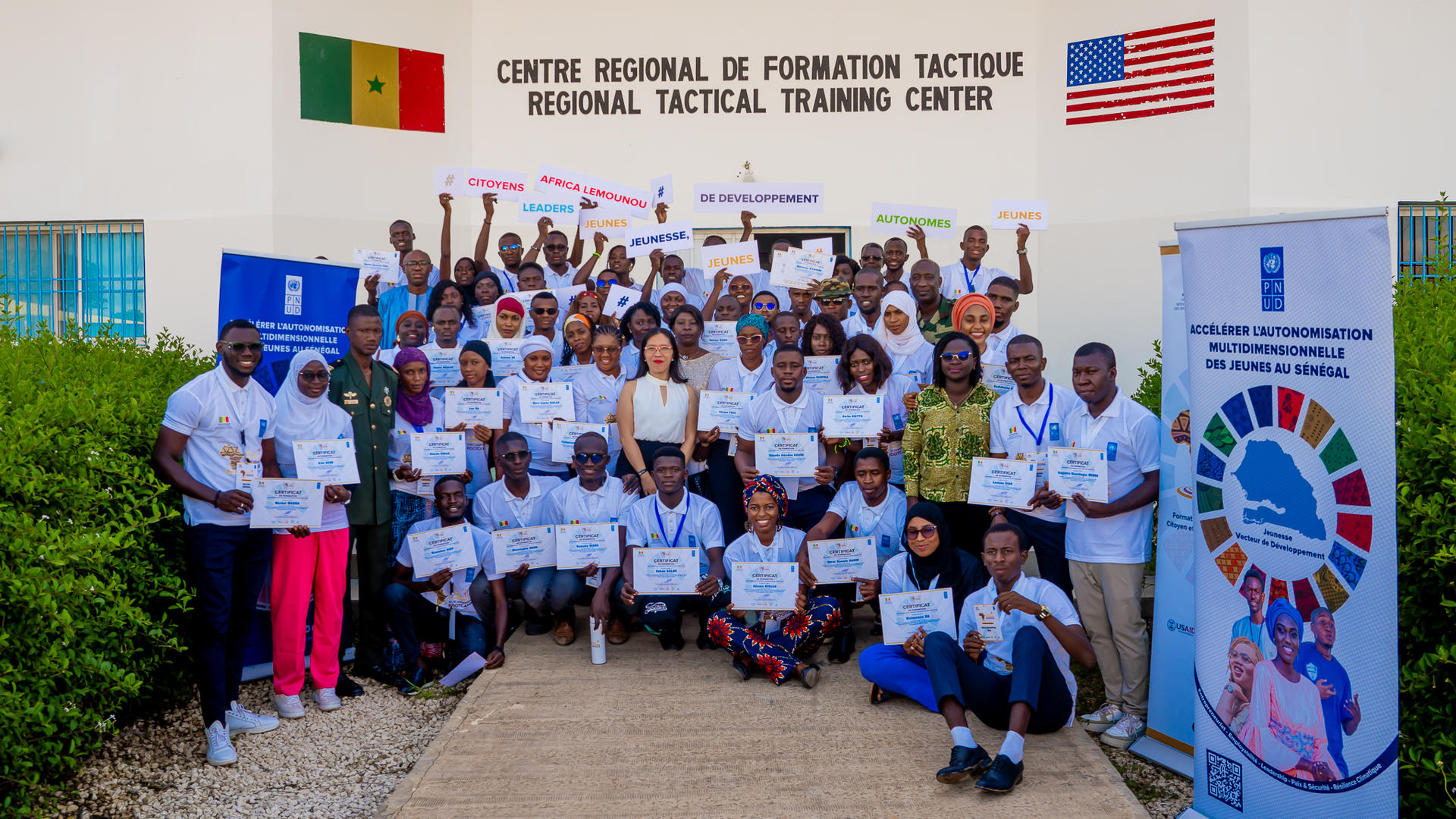 Group photo of trainees holding certificates in front of a training center building.