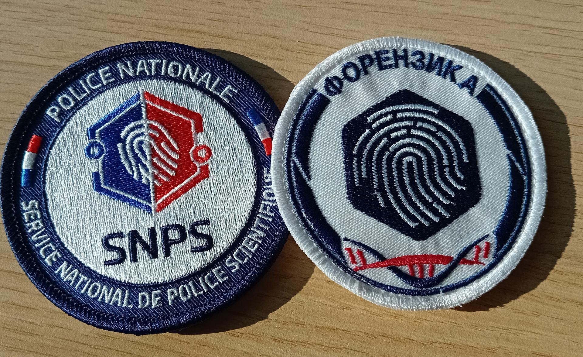 Two embroidered police patches side by side, one in French and one featuring a fingerprint design.