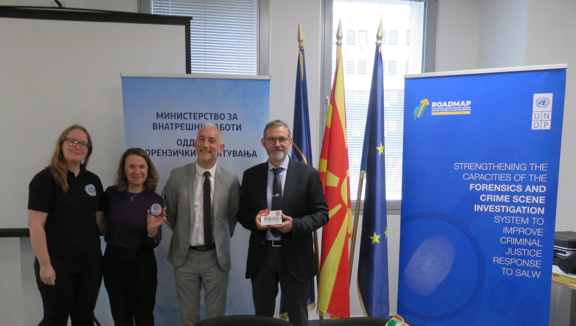 Four professionals stand together in a well-lit office, with flags and banners in the background.