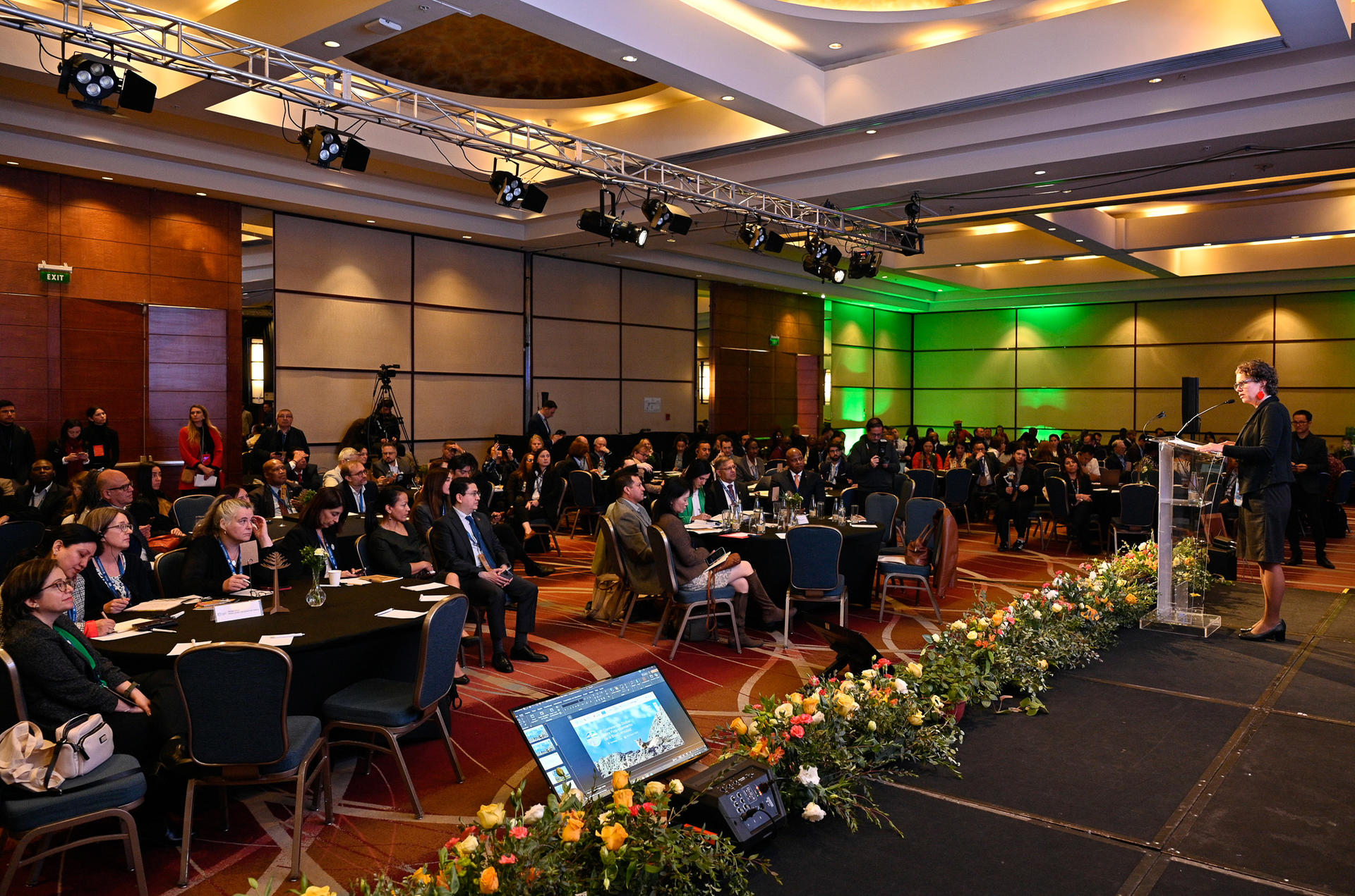 A conference room filled with attendees, focused on a speaker at a podium.