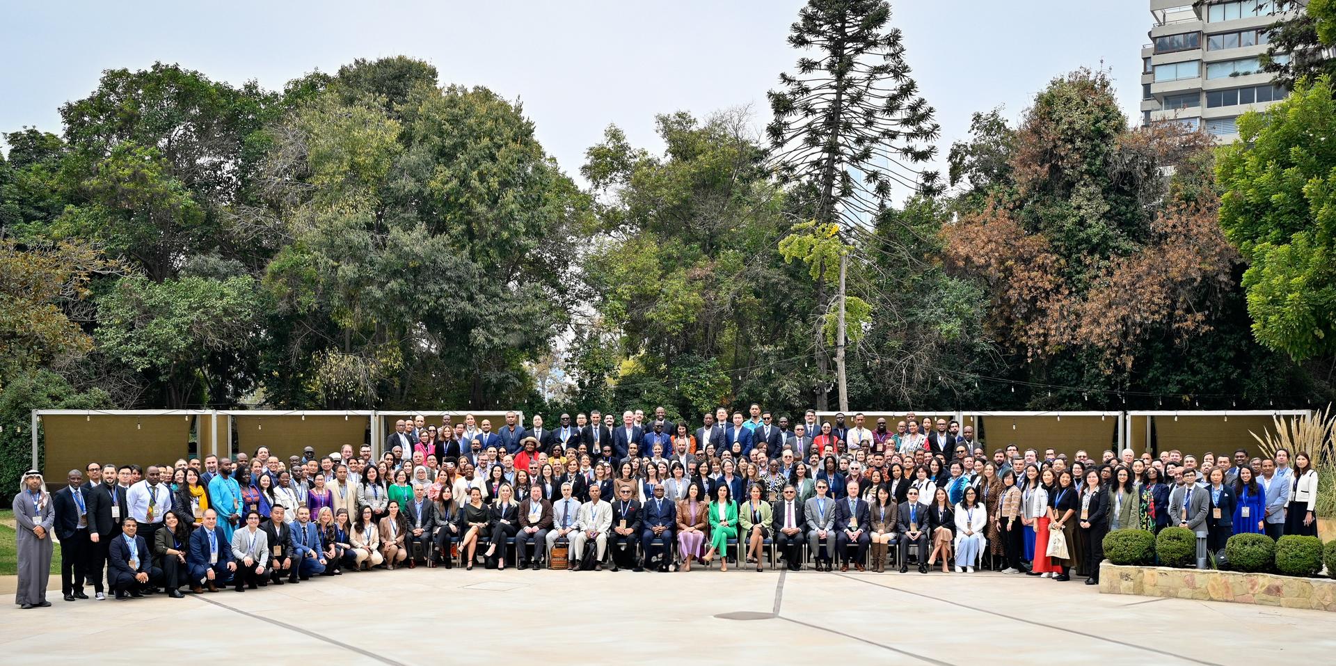 A large group of diverse people standing outdoors in a park setting, smiling for the photo.