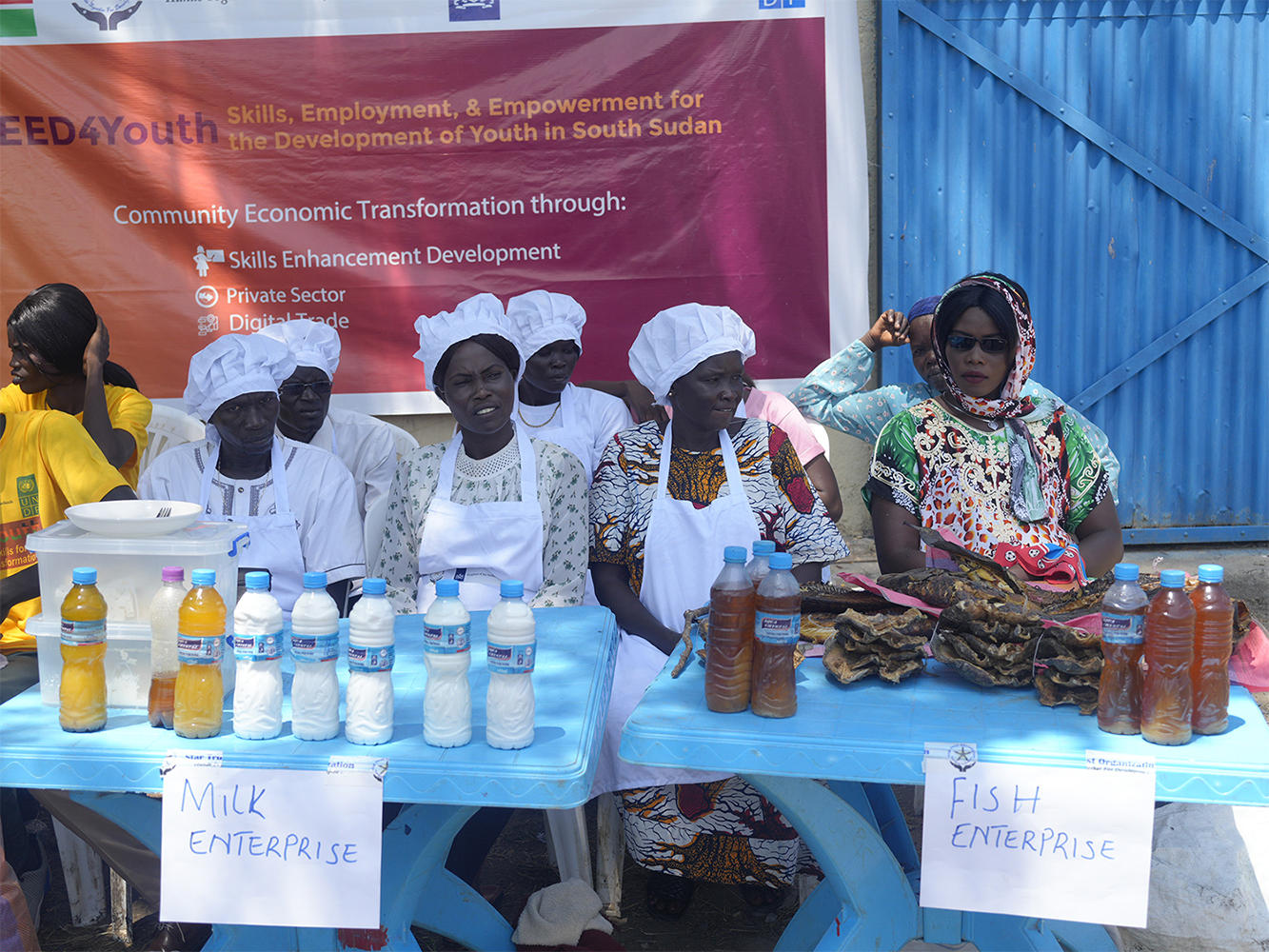 Women in traditional attire seated at a table displaying milk and fish products.