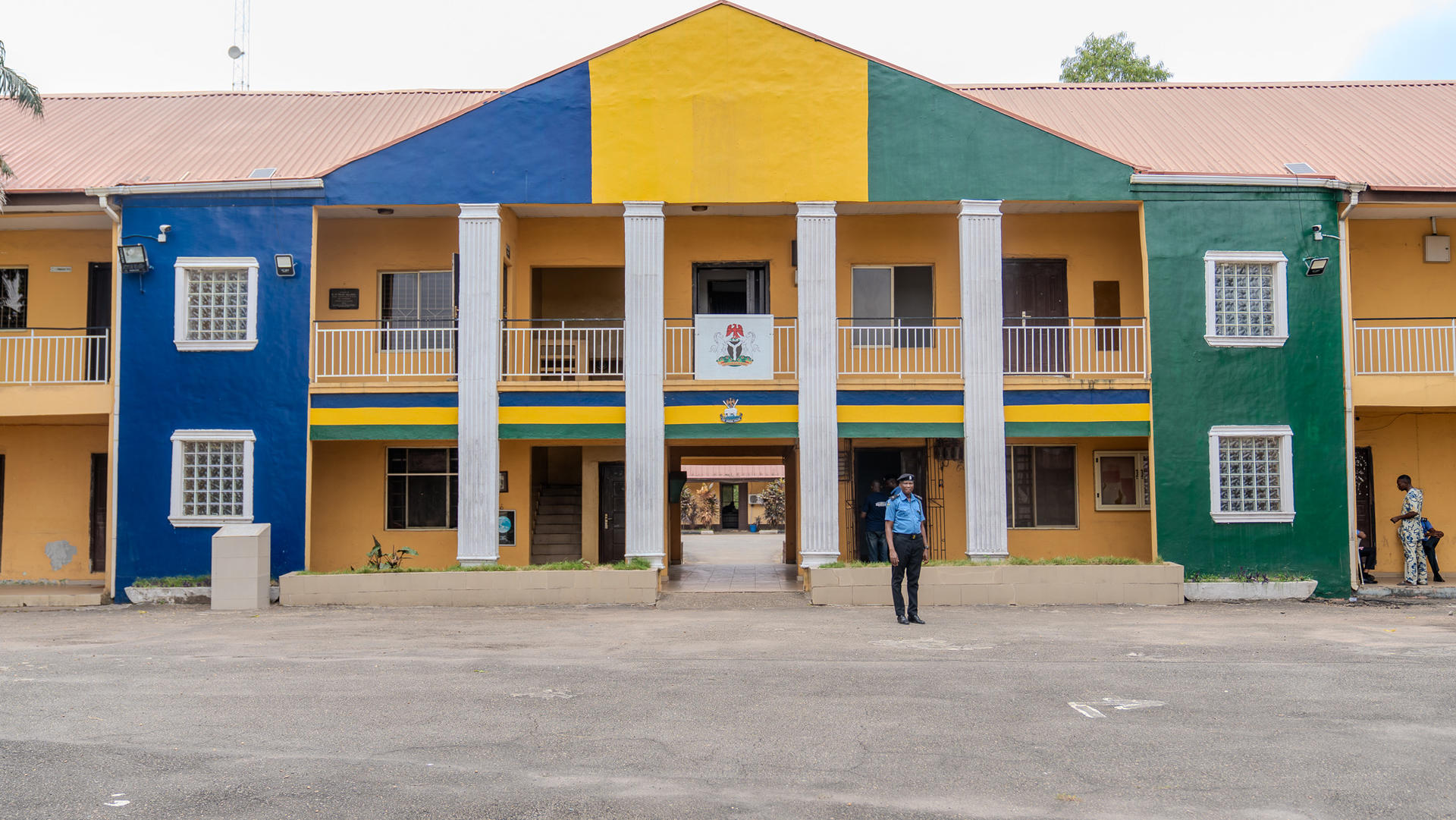 Two-story building painted in blue, green, yellow, and beige with people standing outside.