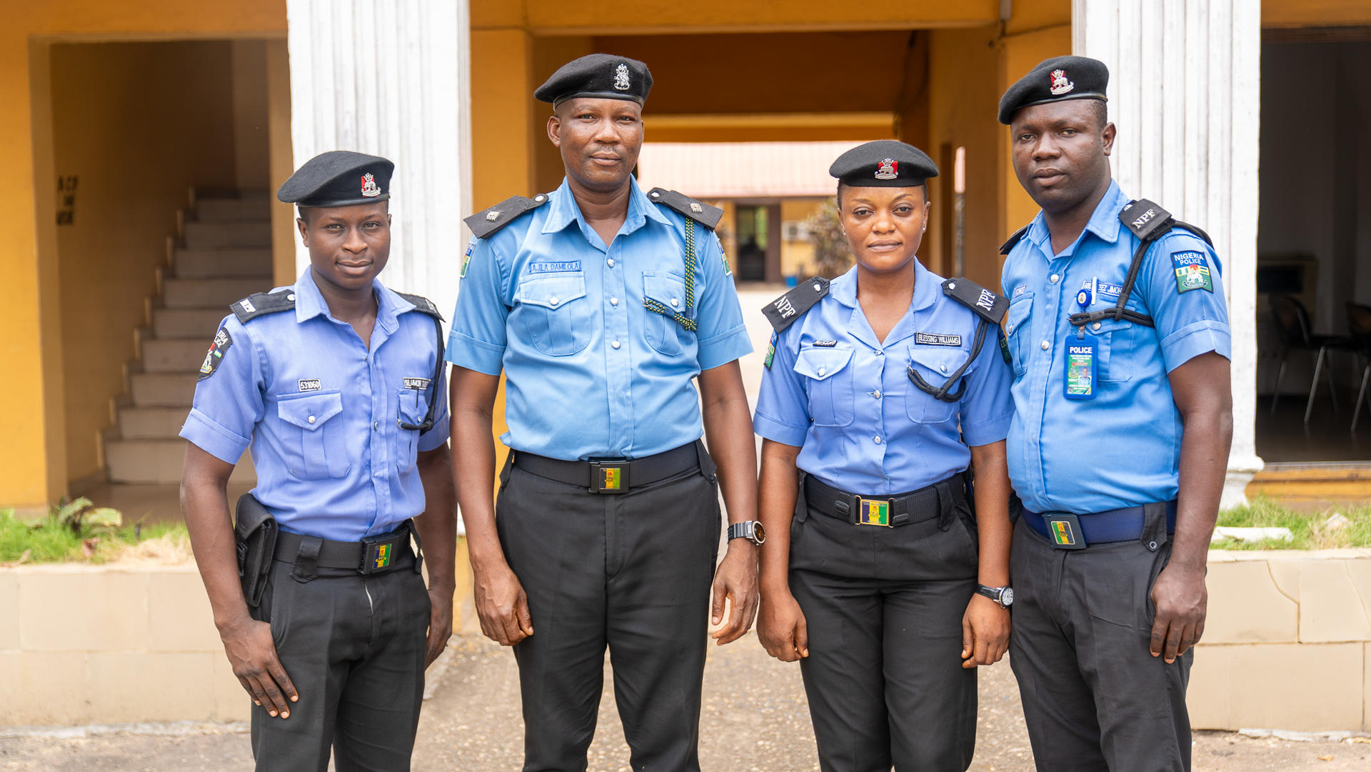 Four police officers in uniform stand together outside a building, smiling at the camera.