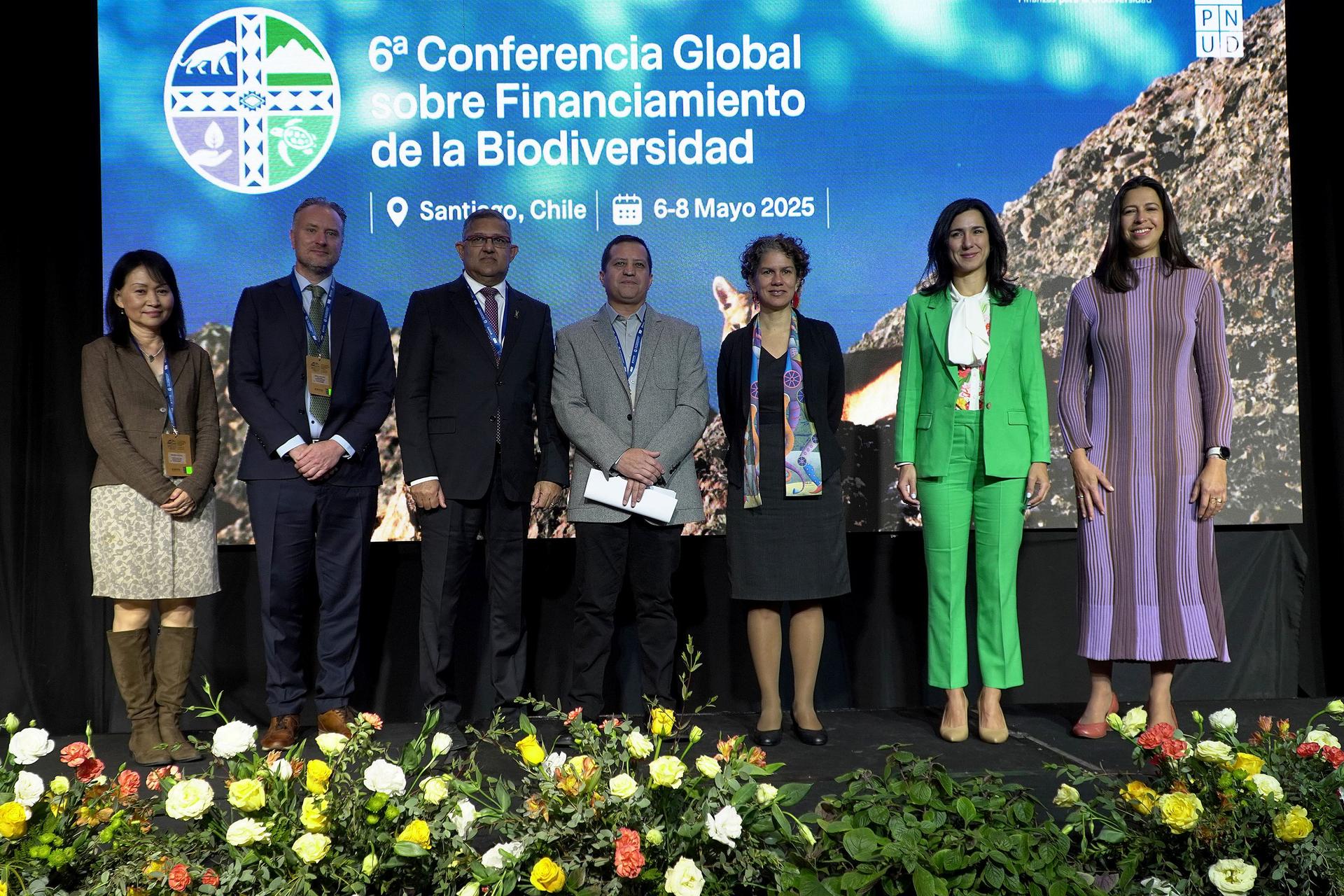 Seven professionals stand together on a stage with a floral backdrop, smiling.