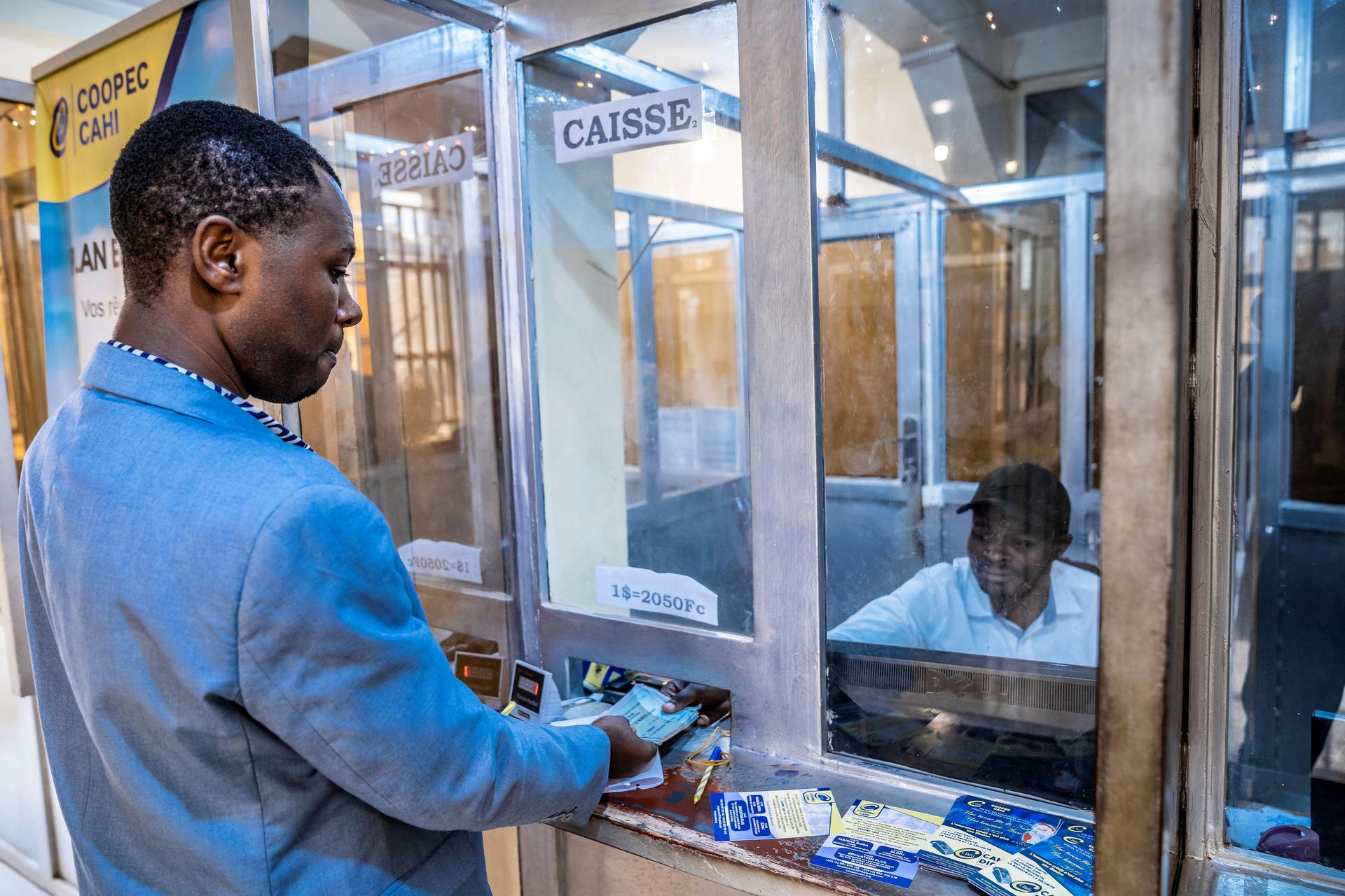 A man in a suit is handing over cash to a clerk through a window at a service counter.