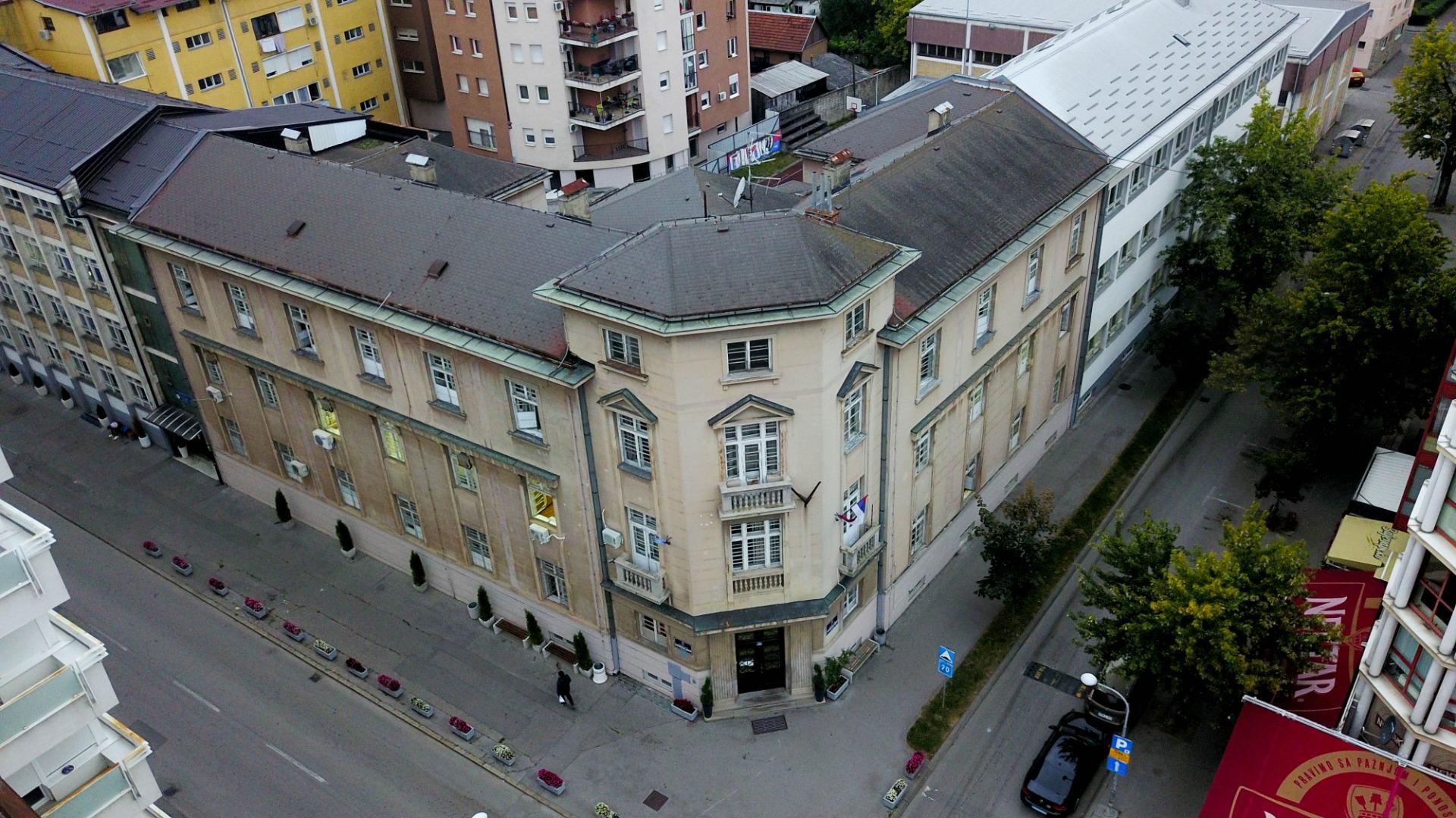 Aerial view of a historic building at a street intersection, surrounded by modern buildings.