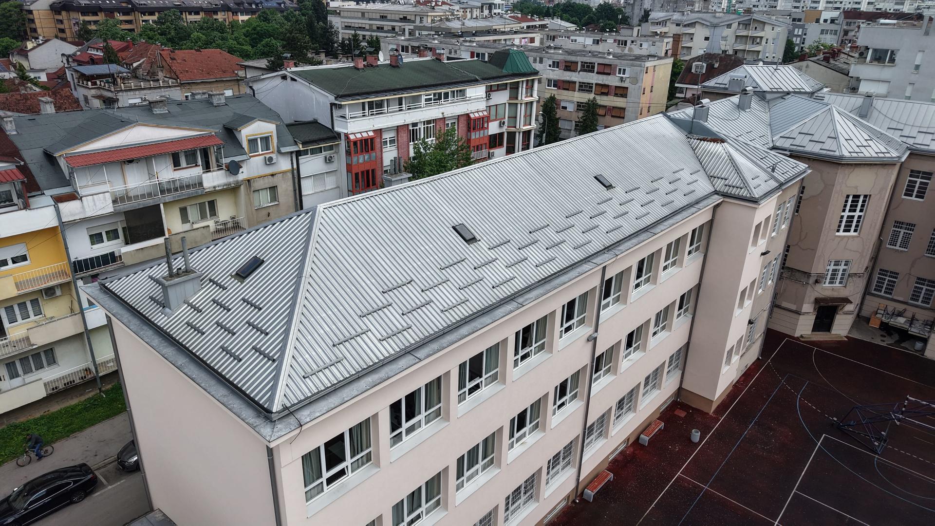 Aerial view of a school building with a sloped roof and surrounding urban landscape.