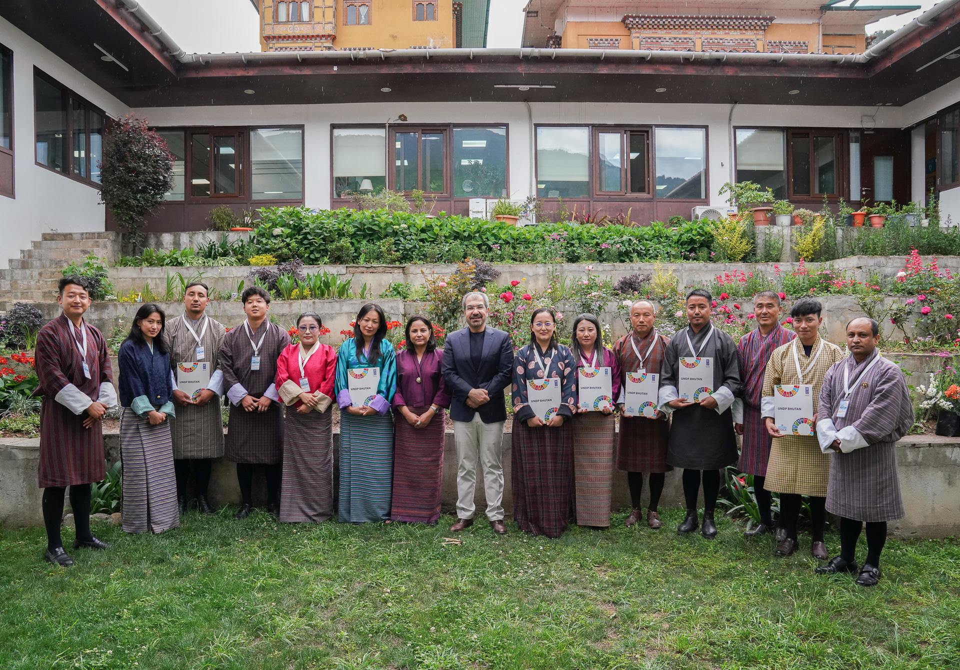 Group of people in traditional attire posing together in a garden setting with flowers.