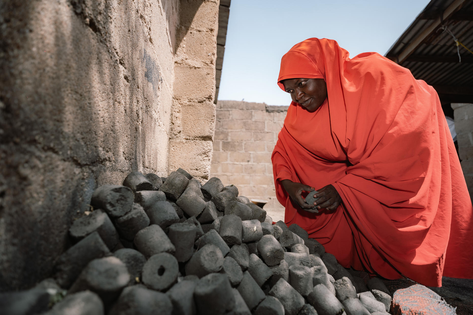 A person in an orange robe examines a pile of black stones near a stone wall.