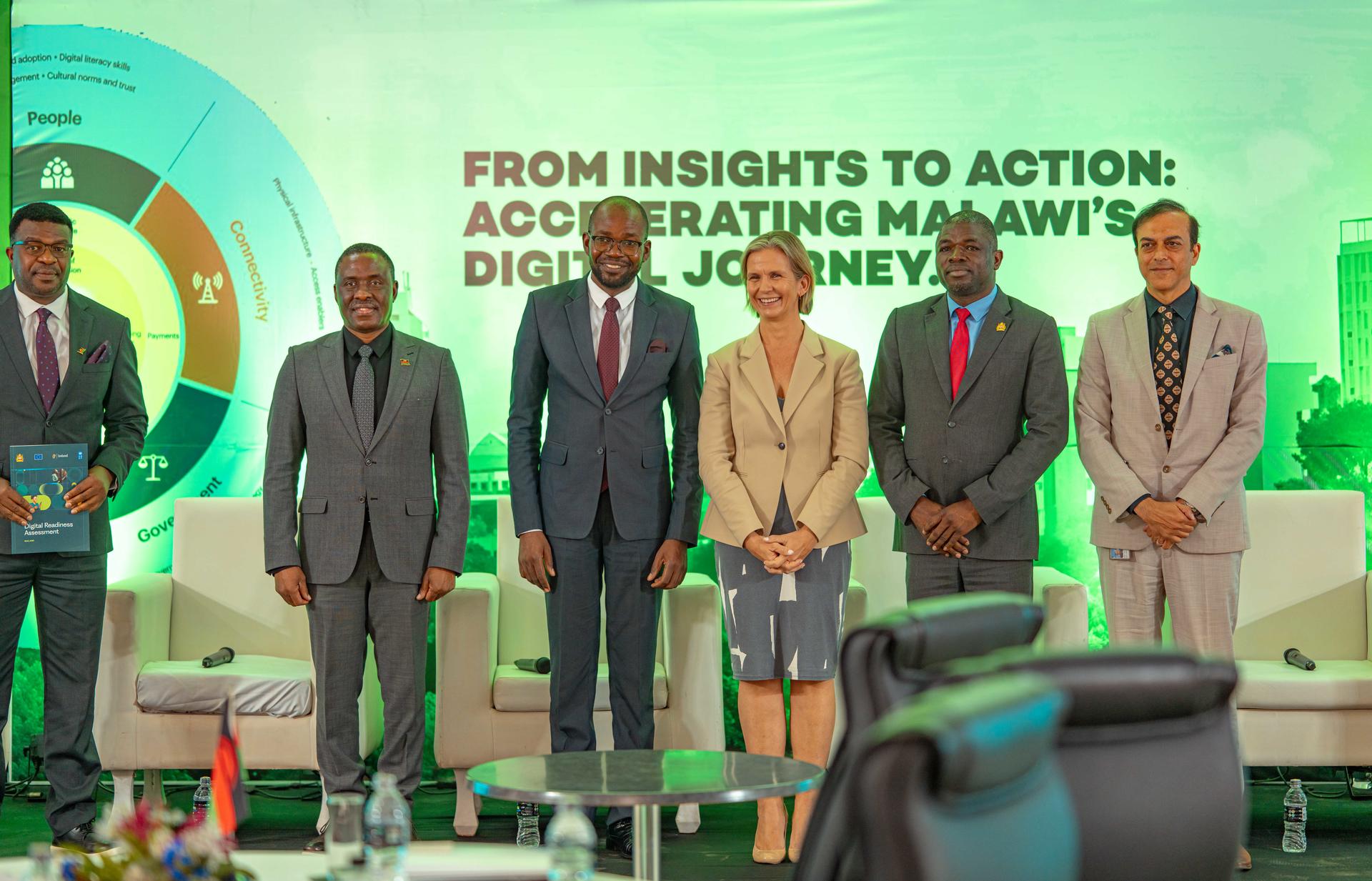 Six professionals stand together on stage, smiling against a colorful backdrop at a conference.