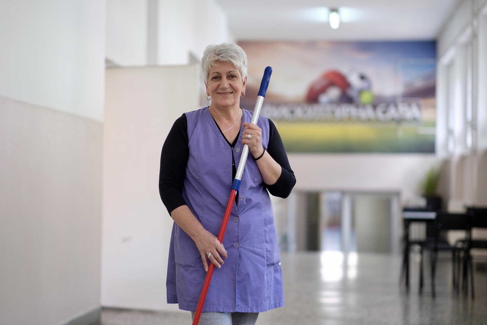 Smiling woman with gray hair holding a white cane, walking in a brightly lit hallway.