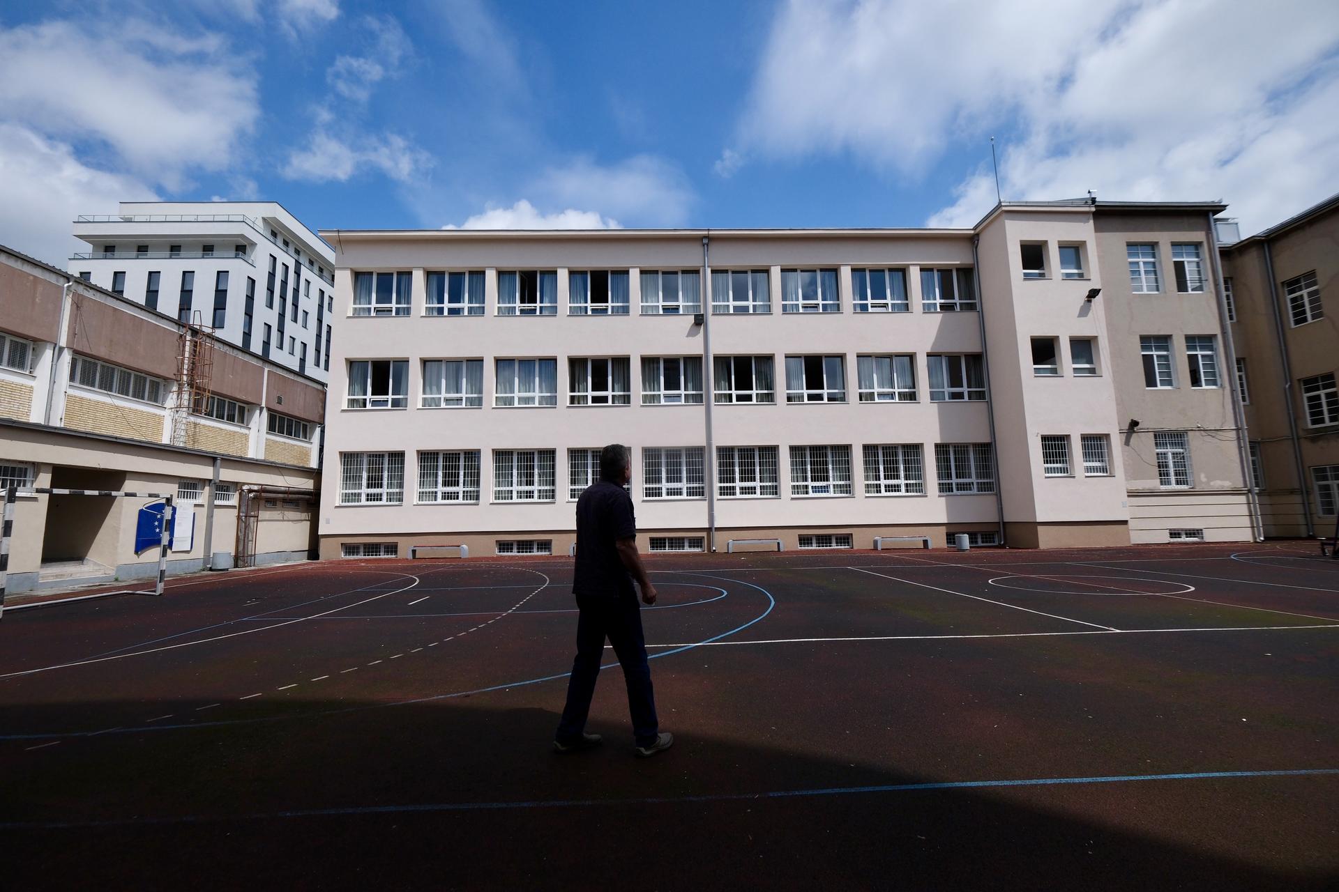 A person walks across a playground in front of a school building under a blue sky.