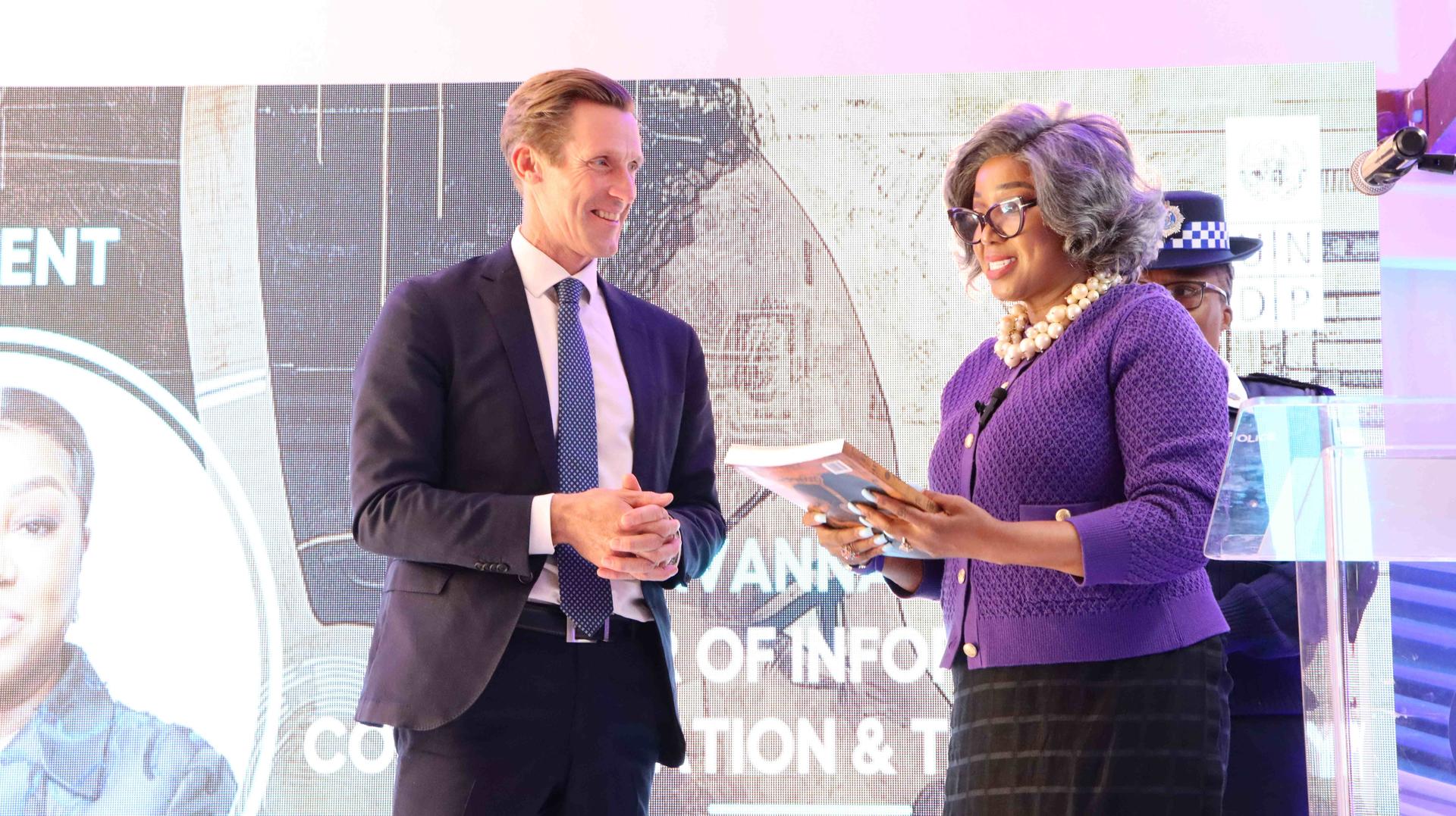 Two speakers at an event engage with each other while standing at a podium.