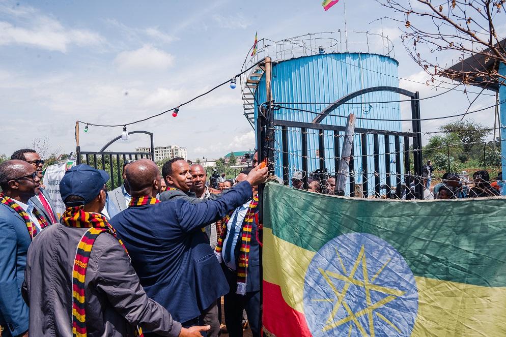 A group of men in suits unveils an Ethiopian flag at a ceremony, with a blue water tank in the background.