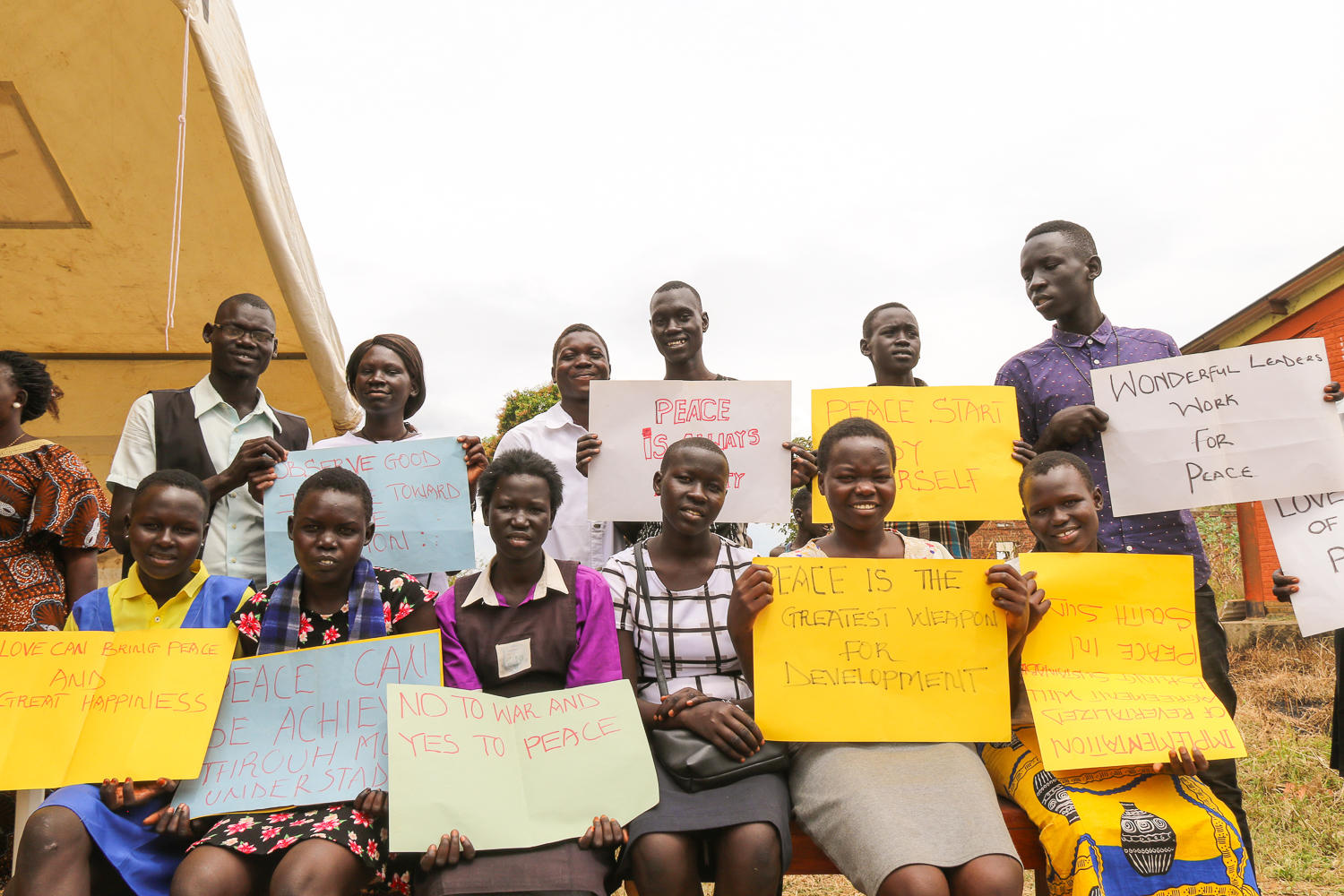 A group of people holding colorful signs, smiling and standing together outdoors.