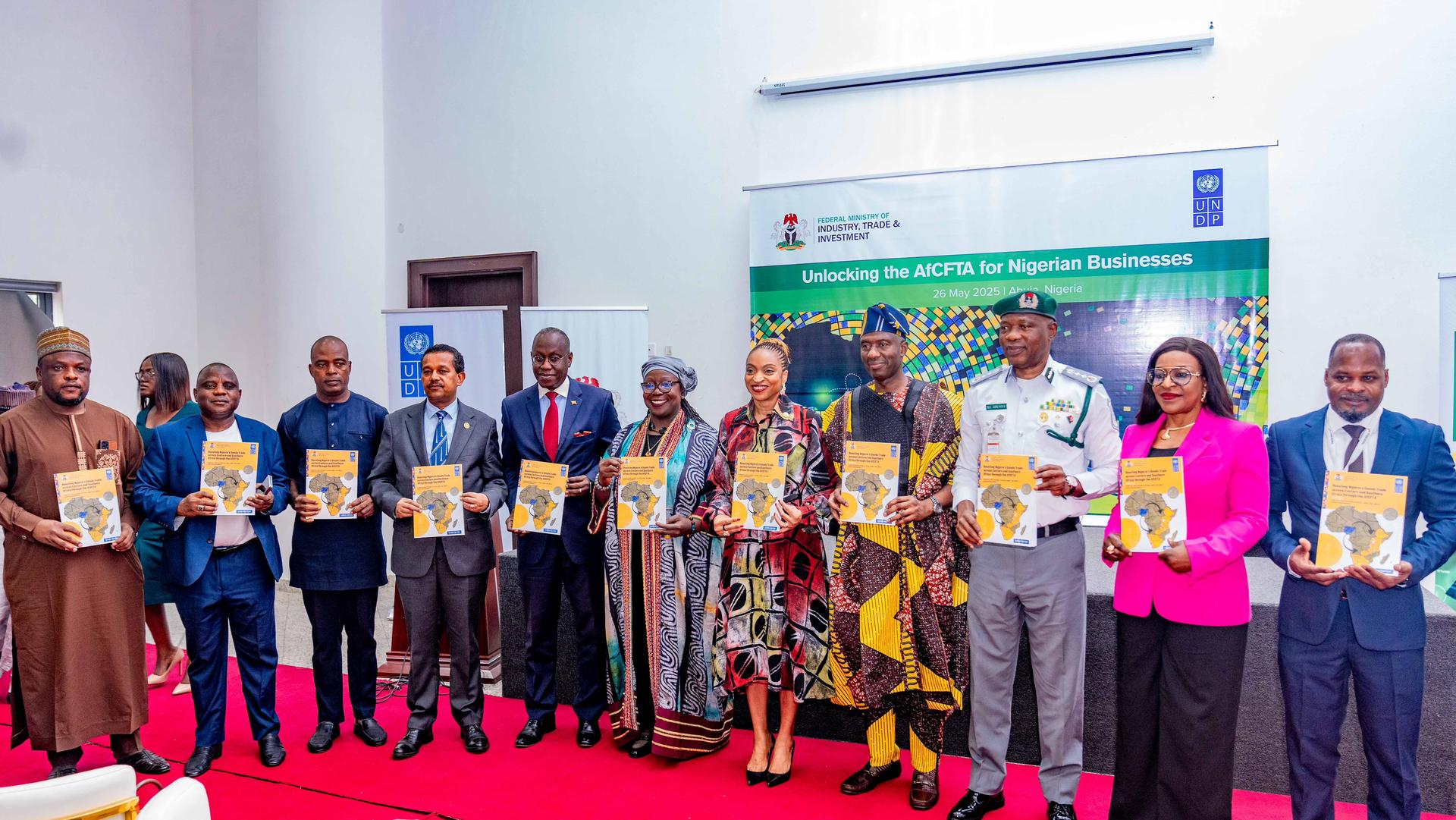A group of people holding documents stands in a formal setting with a colorful backdrop.