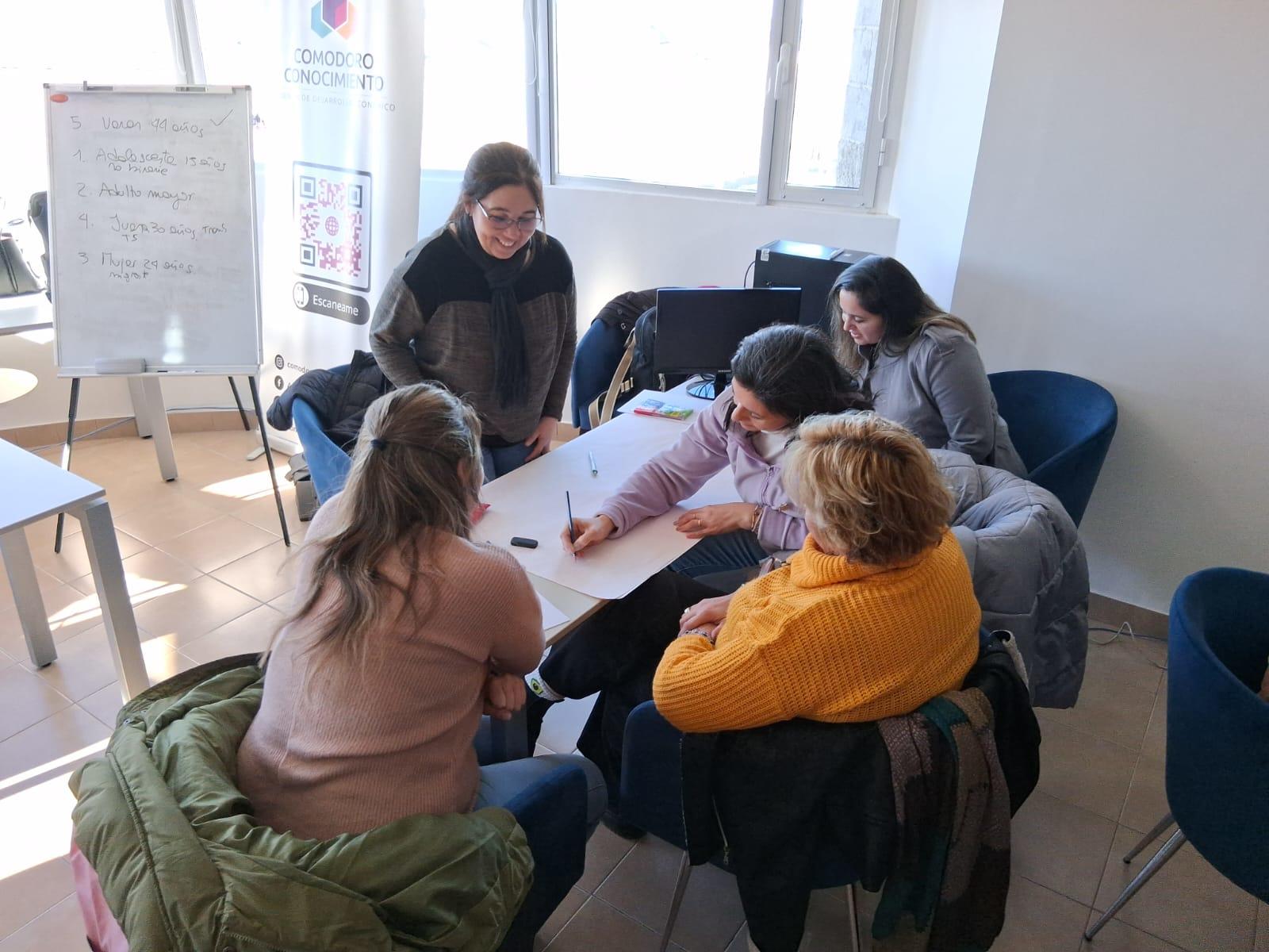 Seis personas sentadas alrededor de una mesa, colaborando mientras discuten y toman nota.