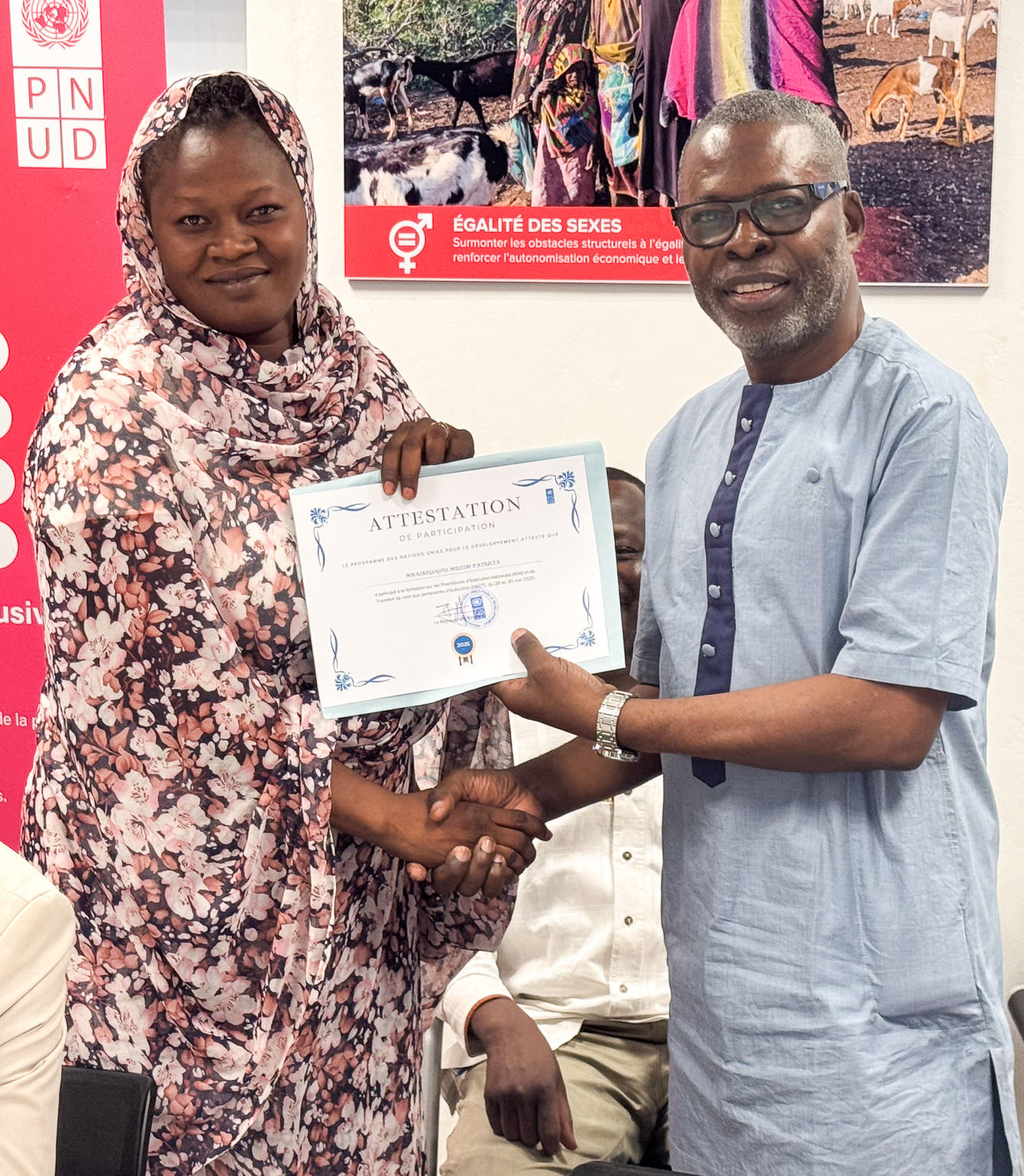 Two people exchanging a certificate, smiling, in a colorful indoor setting.