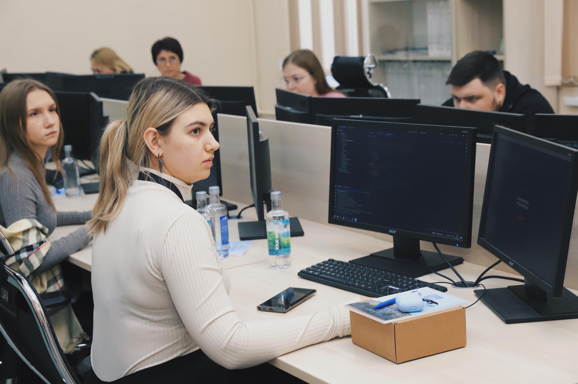 Students in a computer lab, focused on screens, with water bottles and a box on desks.