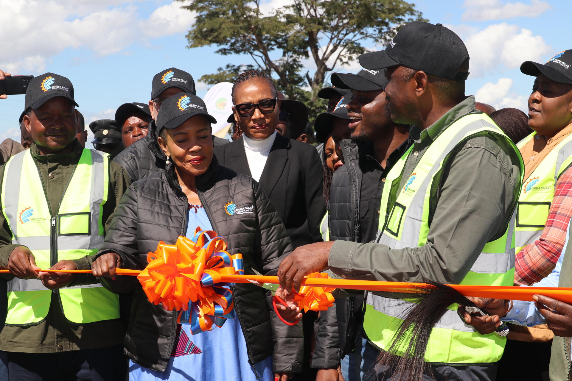 Group of people in safety vests preparing to cut a ribbon at an outdoor event.