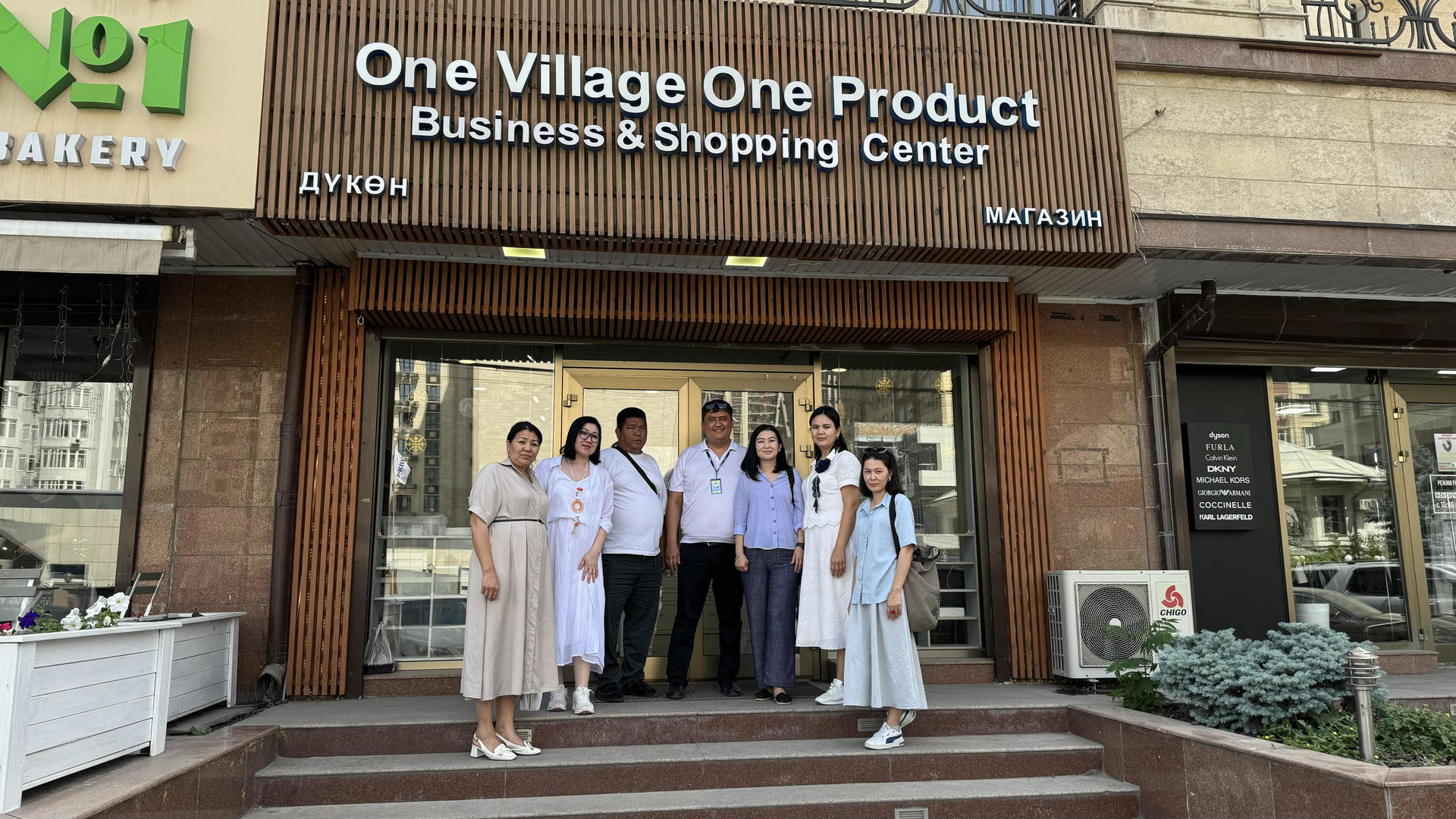 A group of six people stands in front of a business center, smiling.