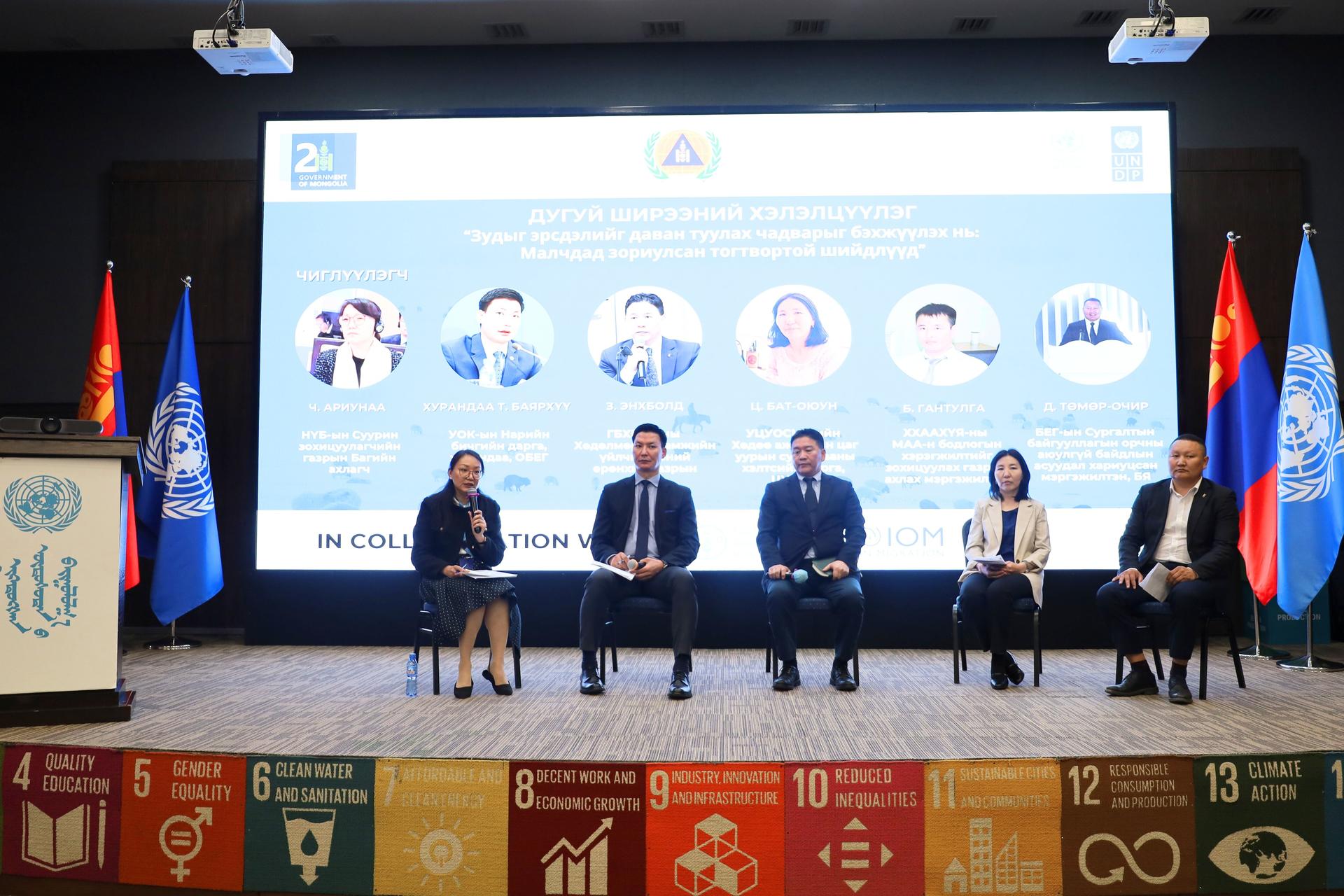 Panel discussion with five speakers on stage, UN flags, and colorful banner below.