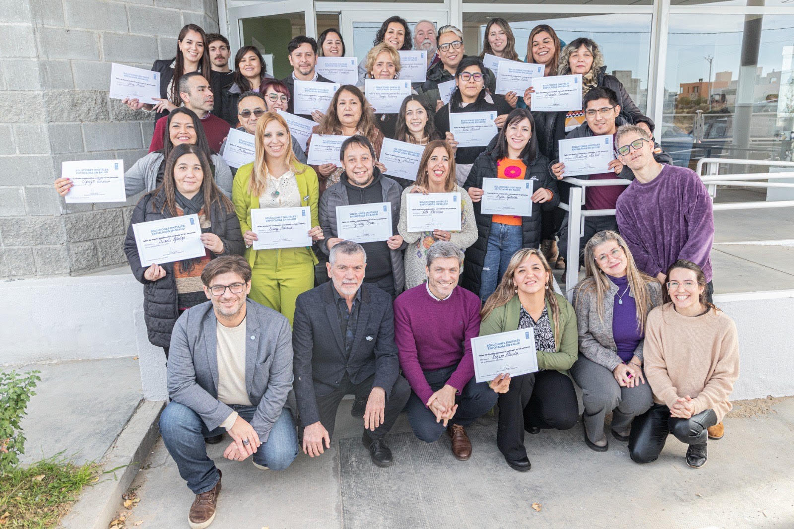 Un grupo de personas sosteniendo certificados mientras posan juntas frente a un edificio.