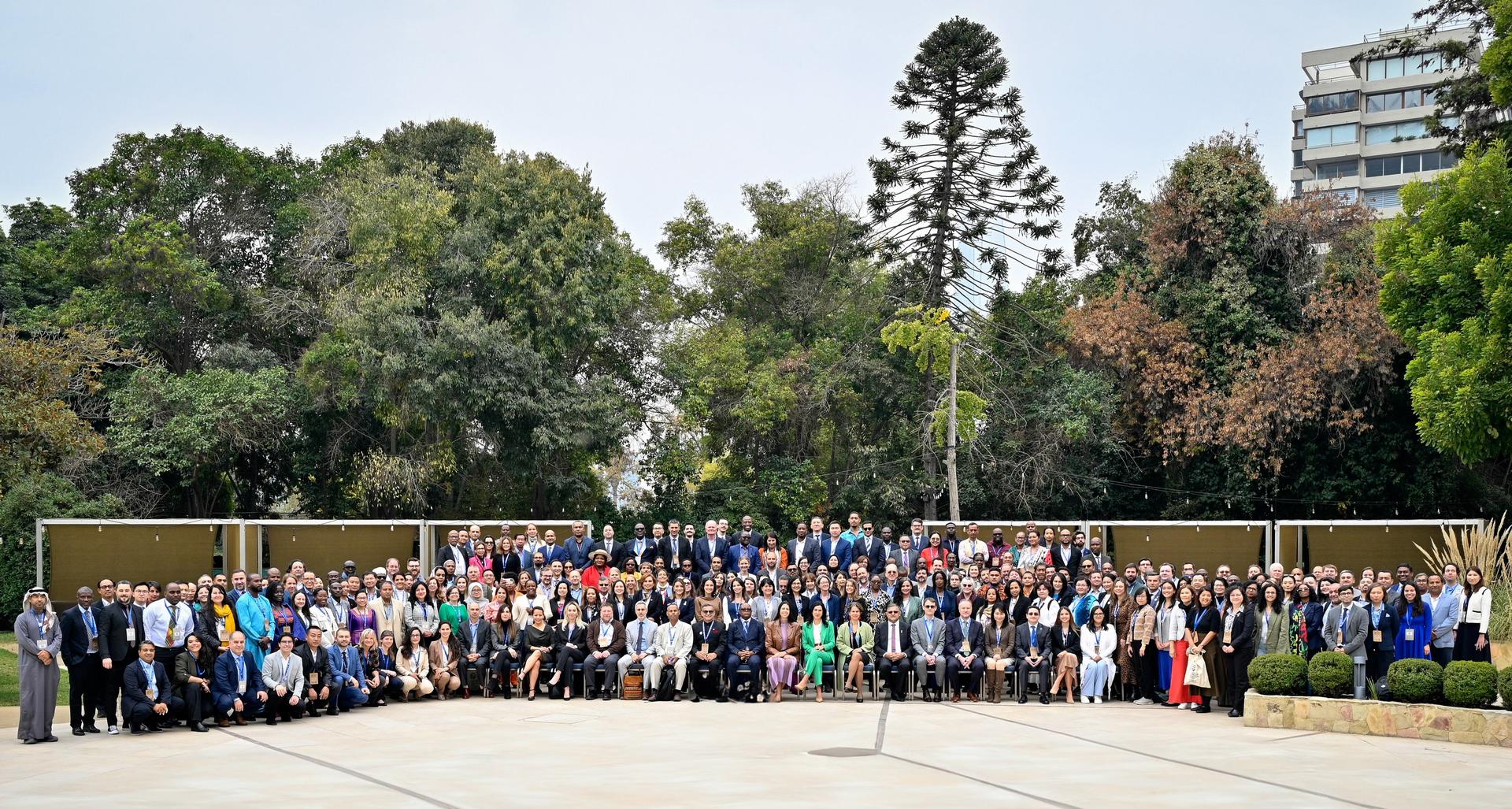 A large group of people posing together outdoors, surrounded by trees and buildings.