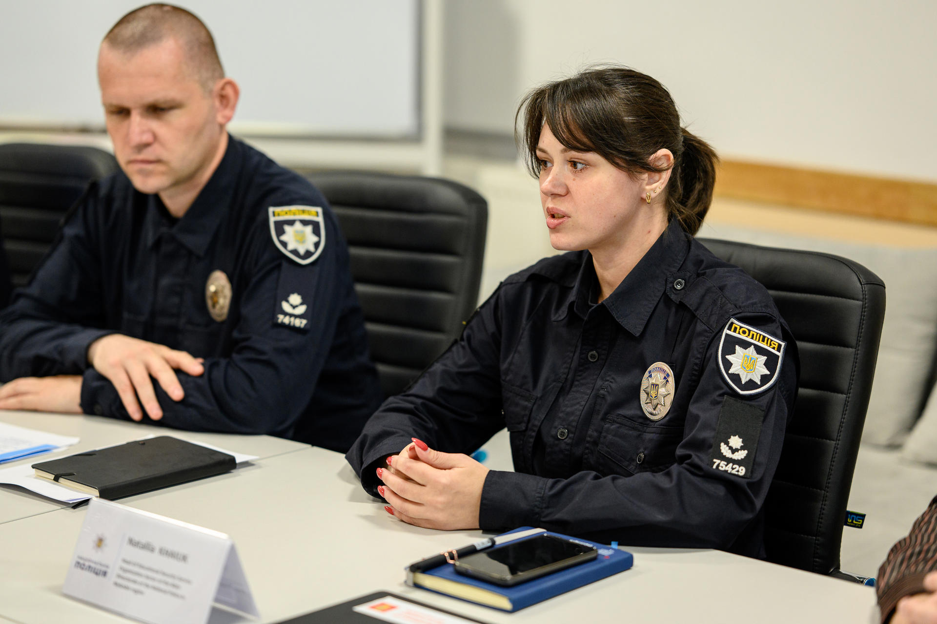 Two police officers in uniform sit at a conference table, discussing serious matters.