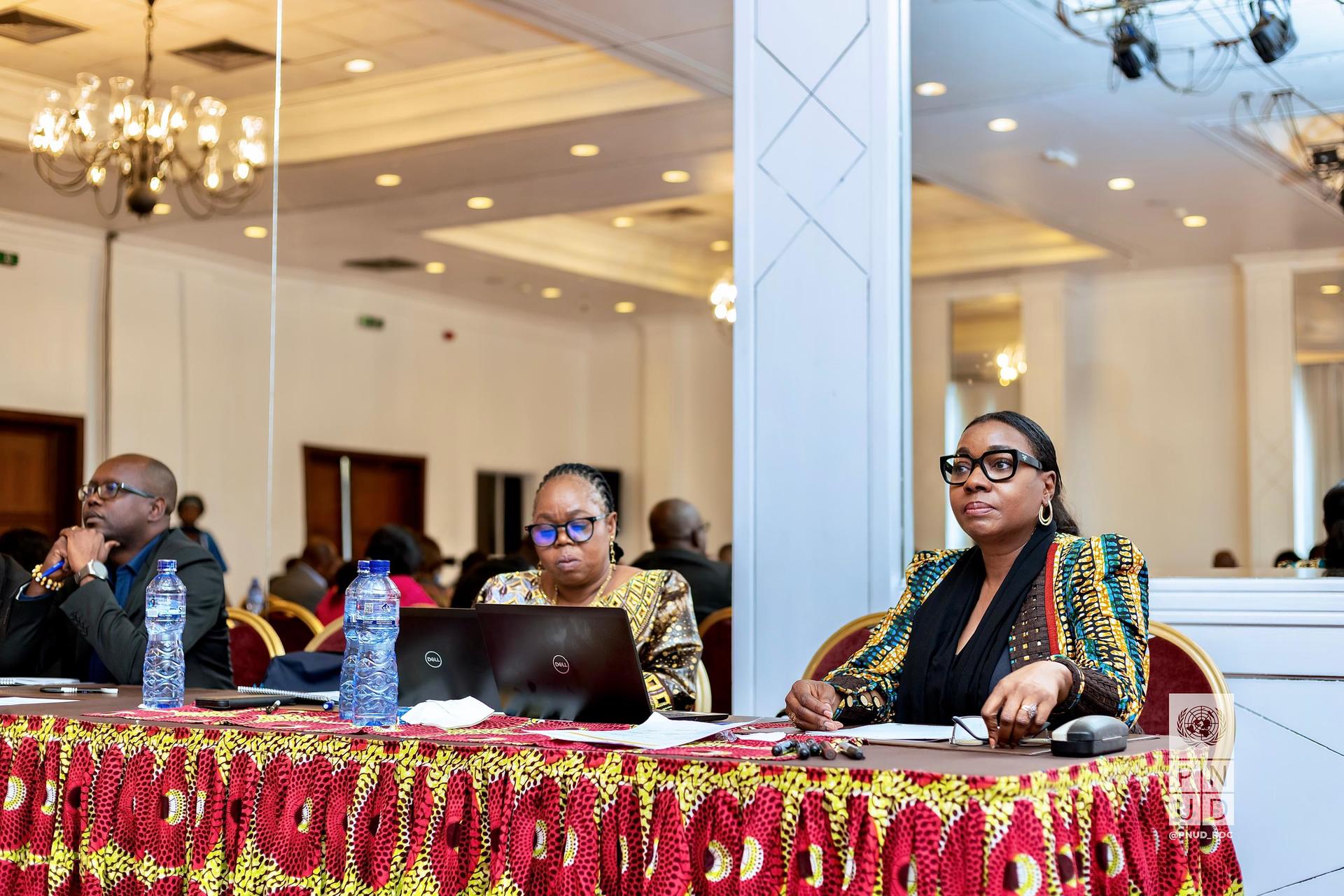Two women in formal attire sitting at a conference table, engaged in discussion.